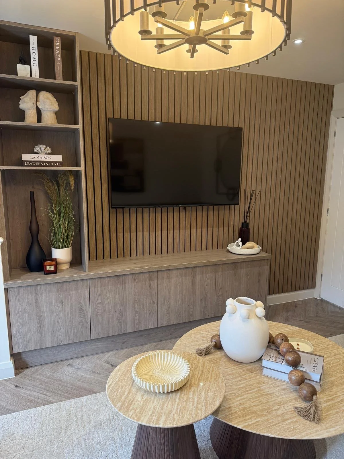 Bespoke wood-slat media wall with open shelving and styled travertine coffee table in a Colwyn Bay show home by The Design House
