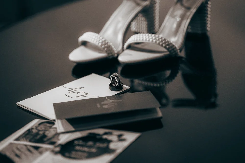 Wedding vow books, wedding invitation, wedding shoes with pearls, and wedding rings on piano at wedding location in Murray Kentucky