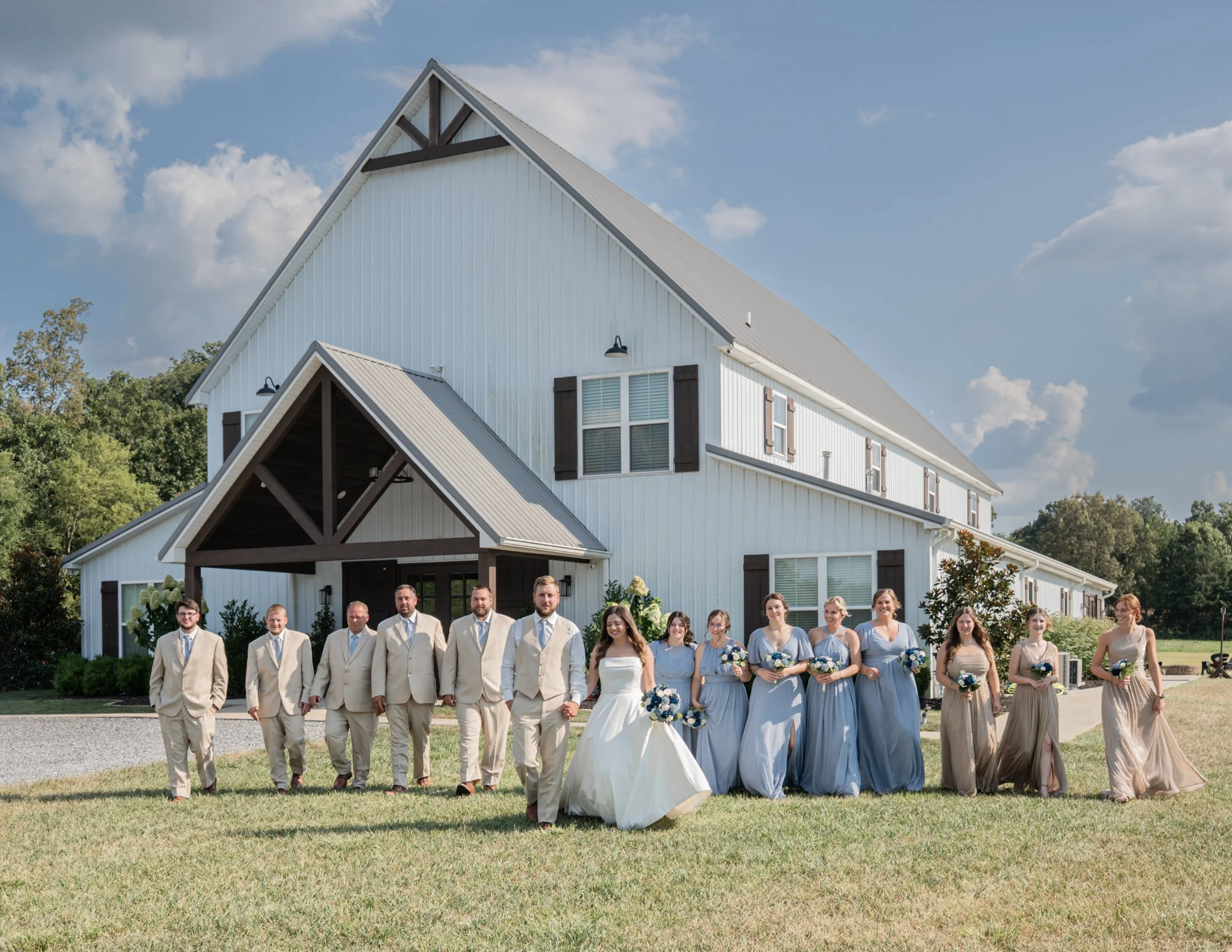 bride and groom with bridal party and groomsmen walking in front of the venue at the Barn at White Oaks wedding venue in Murray Kentucky