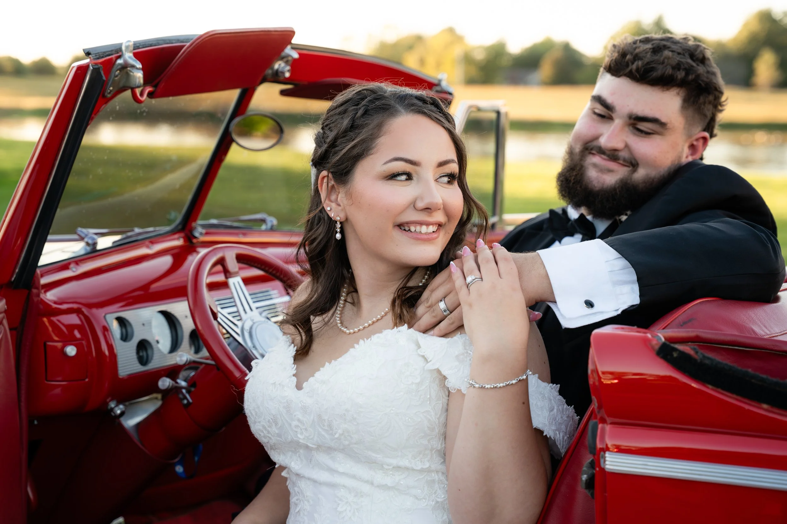 bride and groom photo displaying wedding rings after wedding ceremony with red classic car at sunset in October at the Commonwealth Event Center wedding venue in Paducah Kentucky