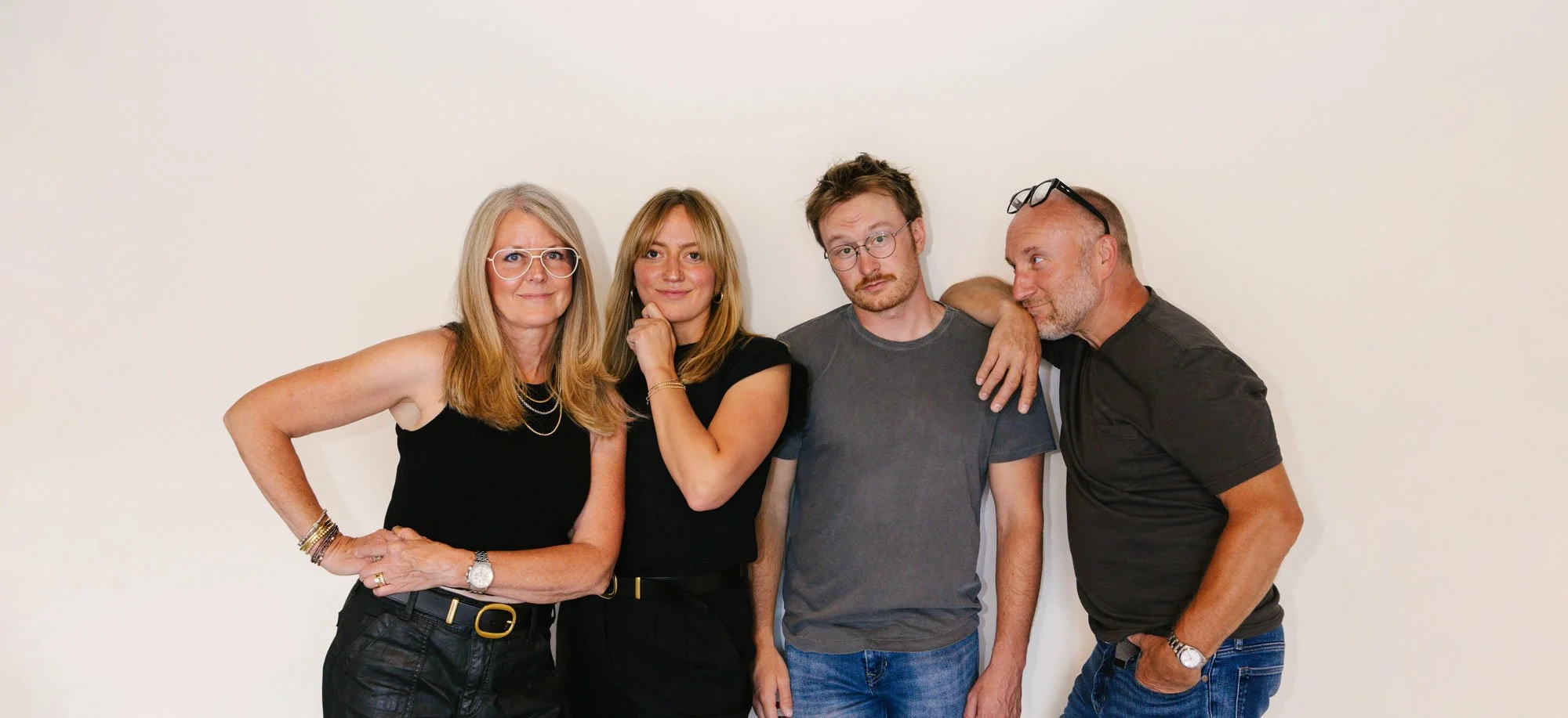 Four people standing close together against a plain white wall, posing for the camera.
