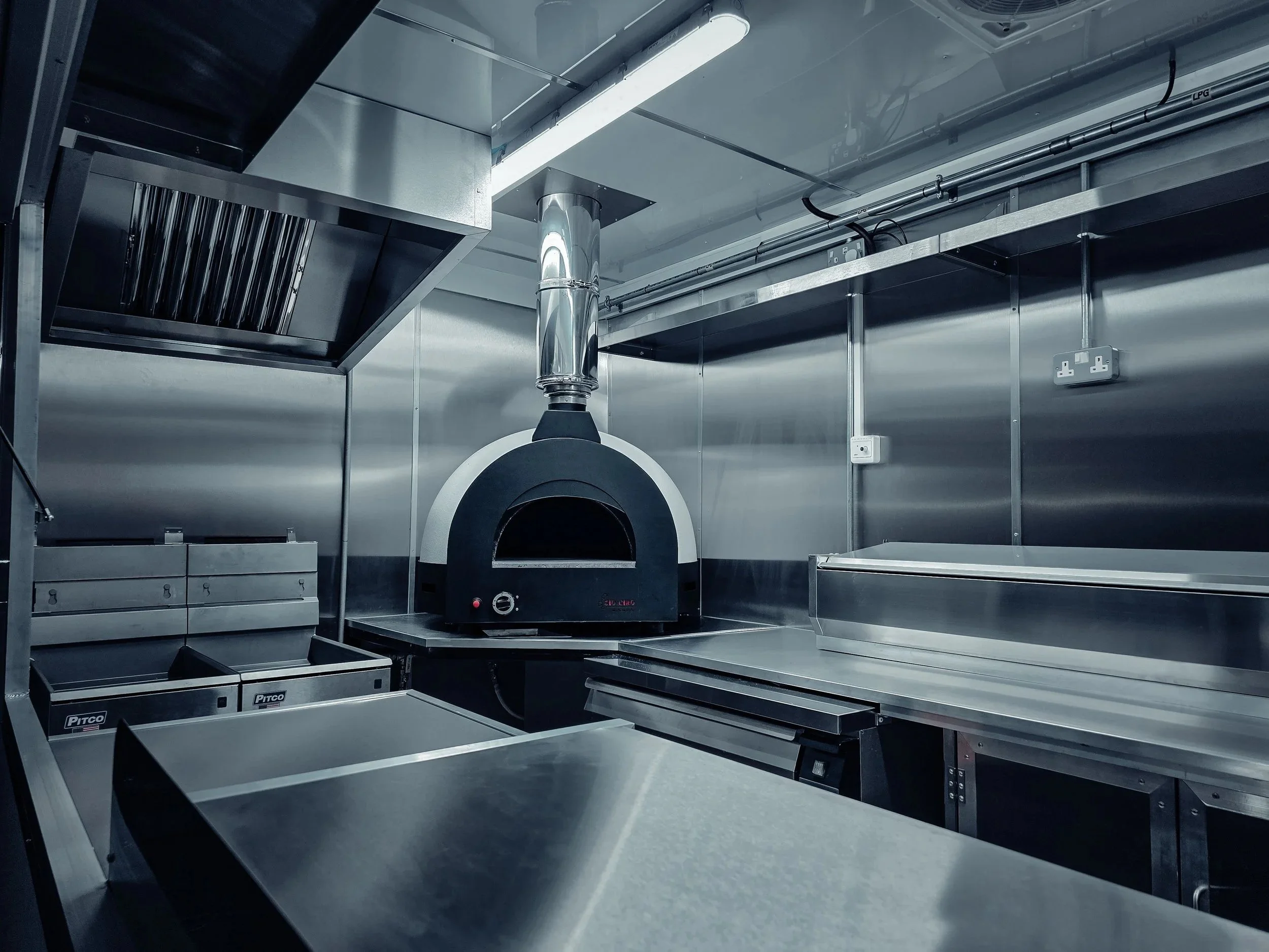 Industrial kitchen with pizza oven in a stainless steel clad food truck conversion.