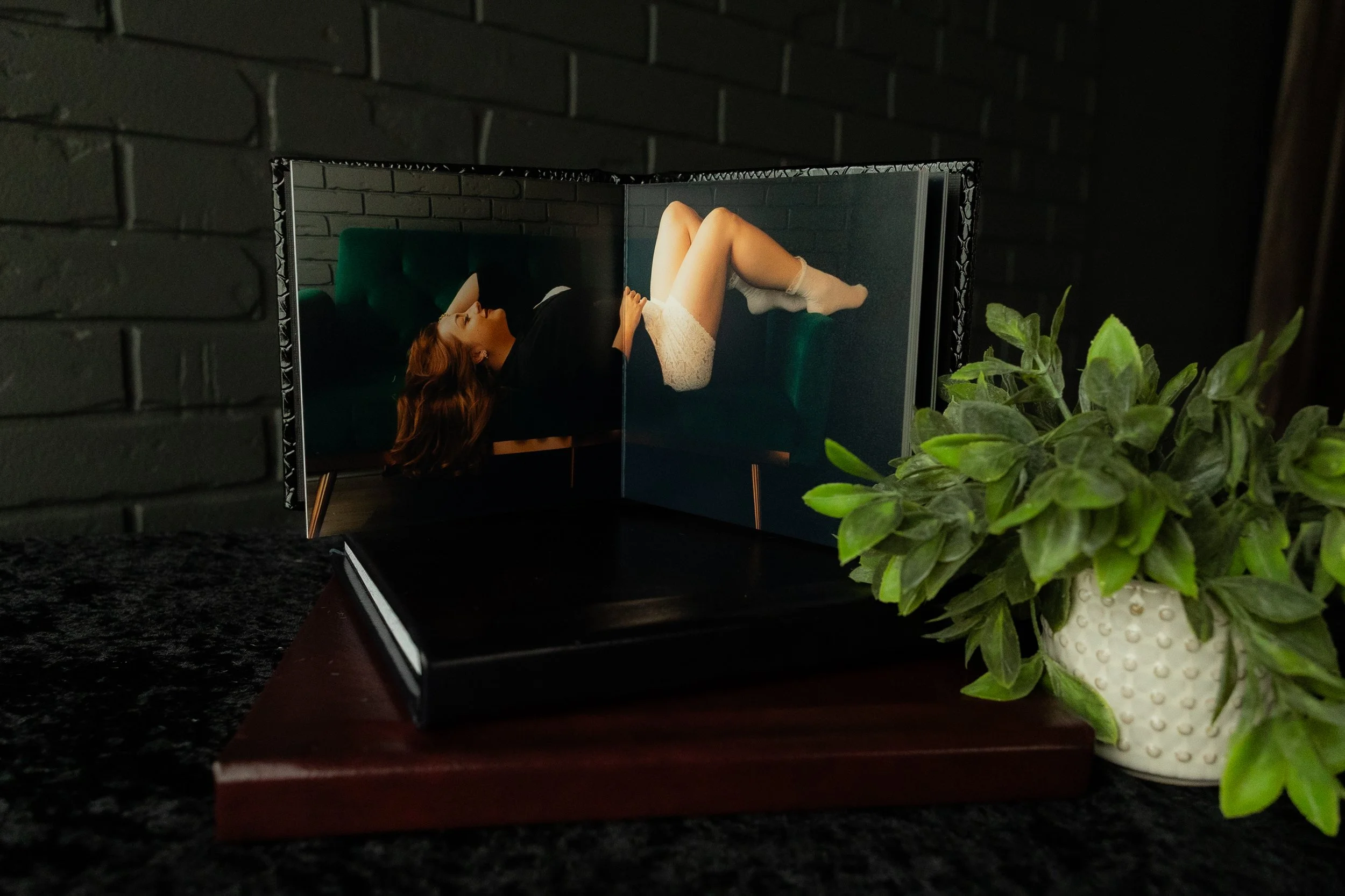 Open boudoir photo album displayed beside a green potted plant.