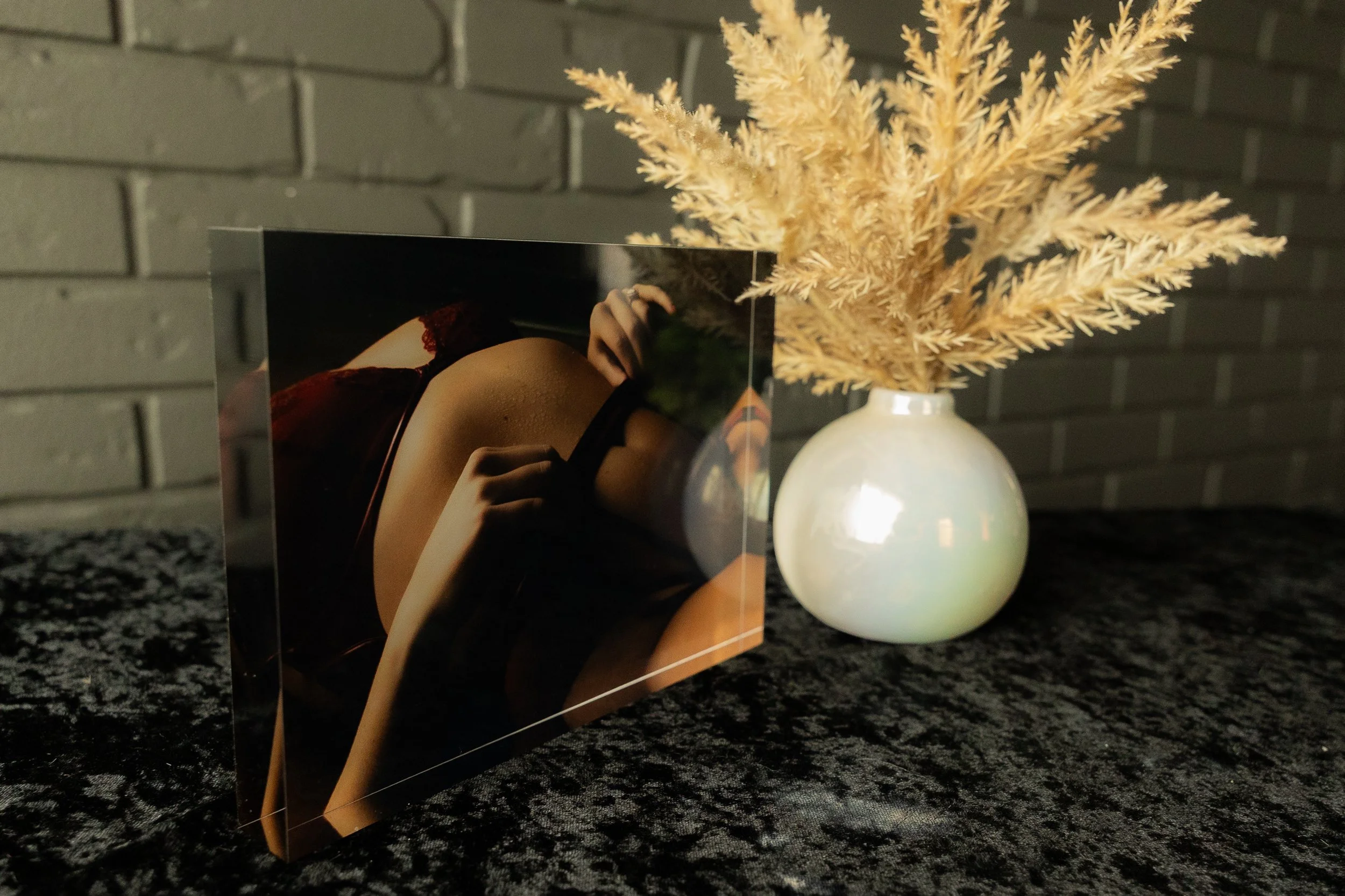 Intimate boudoir photograph displayed in an acrylic block beside a vase of dried foliage.