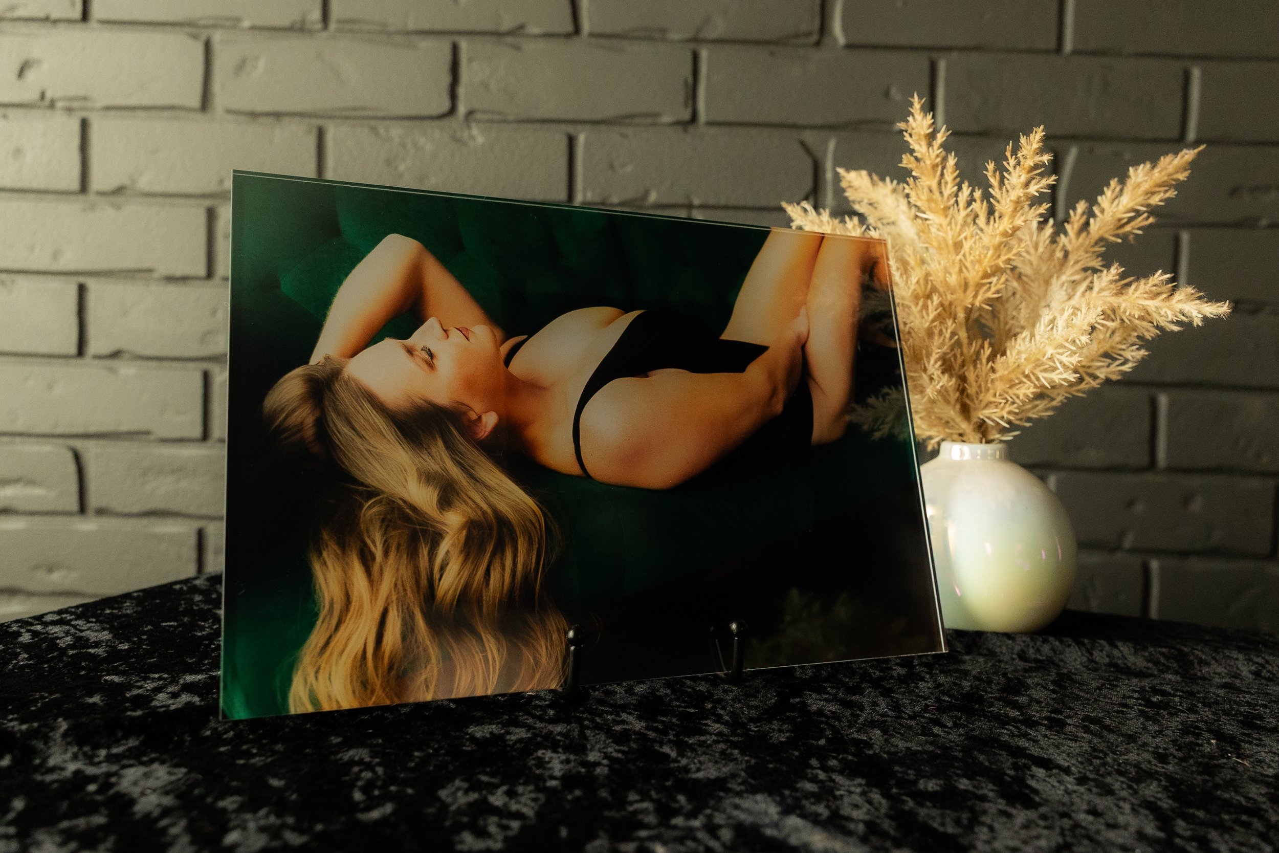 Intimate boudoir photograph displayed in an acrylic block beside a vase of dried foliage.