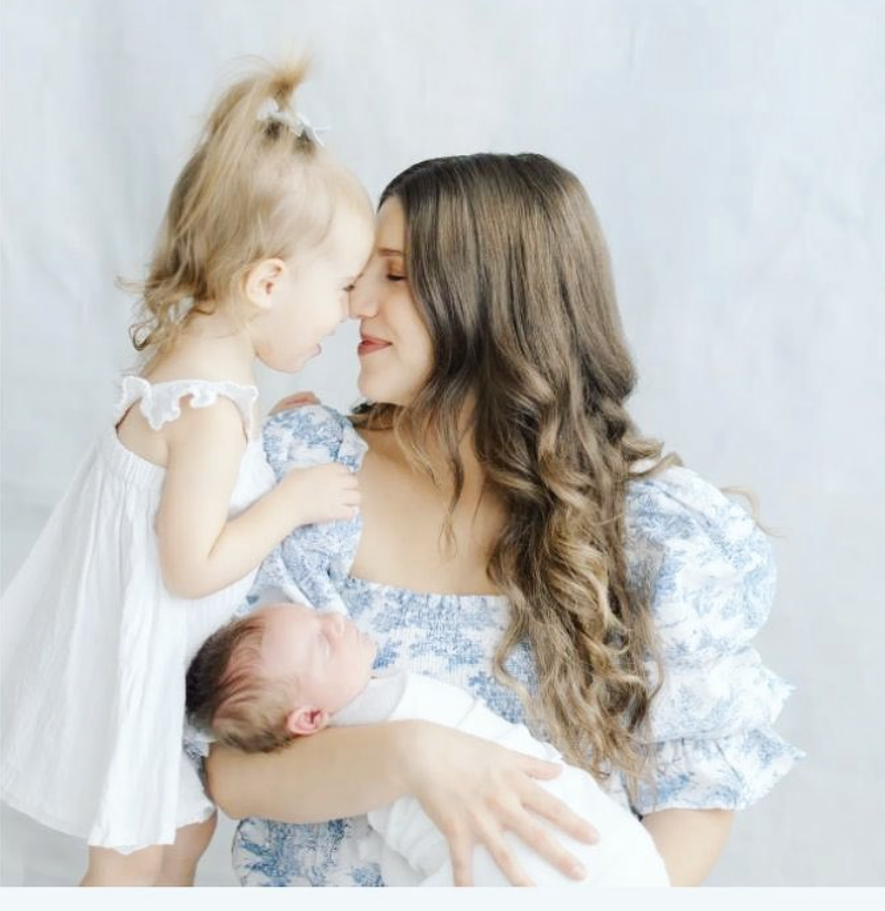 A woman holding a newborn baby and a young girl touching foreheads