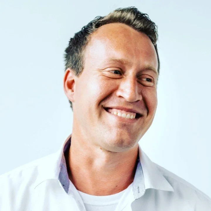 Smiling man in a white shirt looking to his left against a plain light background.