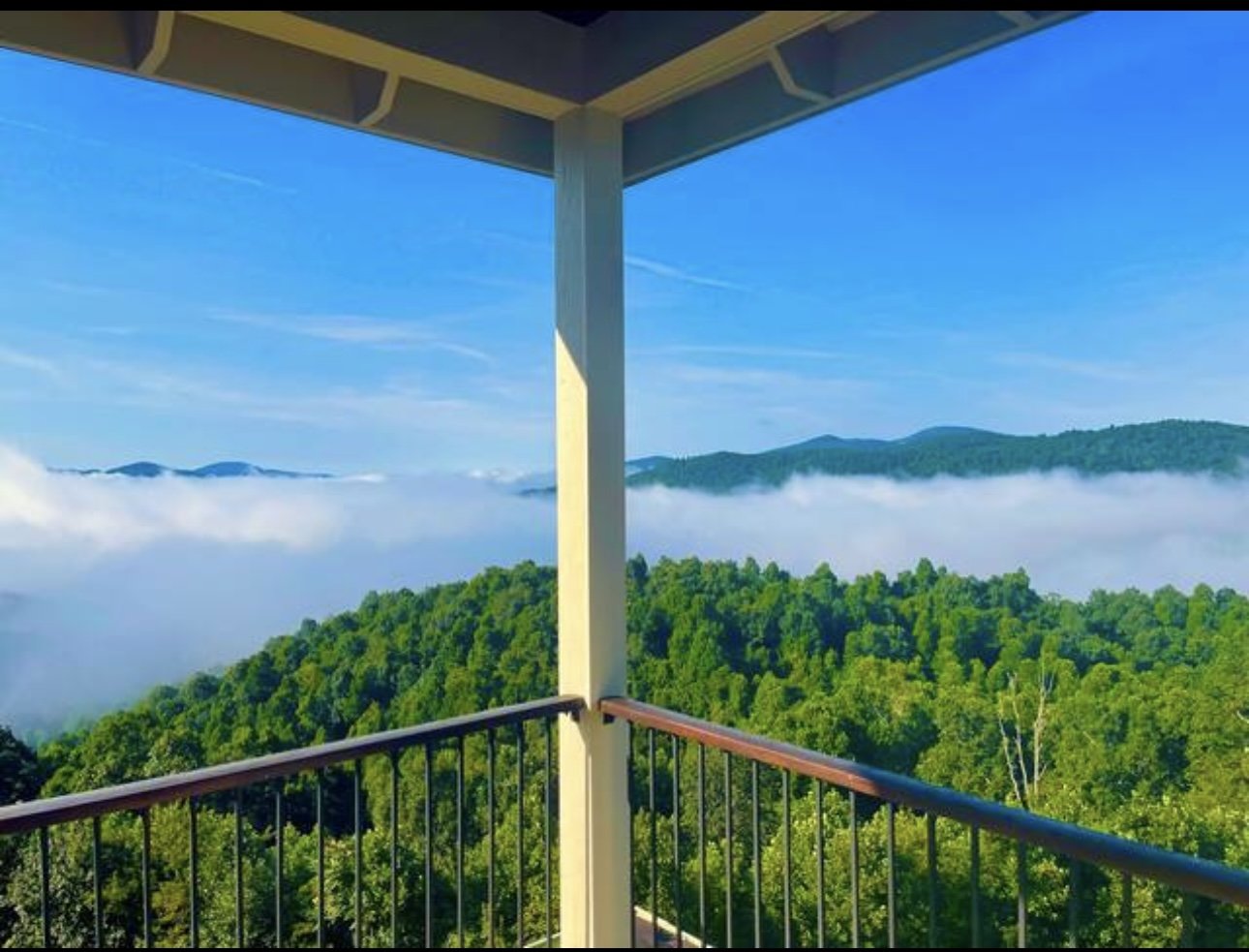 View from a balcony of a lush green forested mountain landscape with a layer of fog and blue sky in the background.