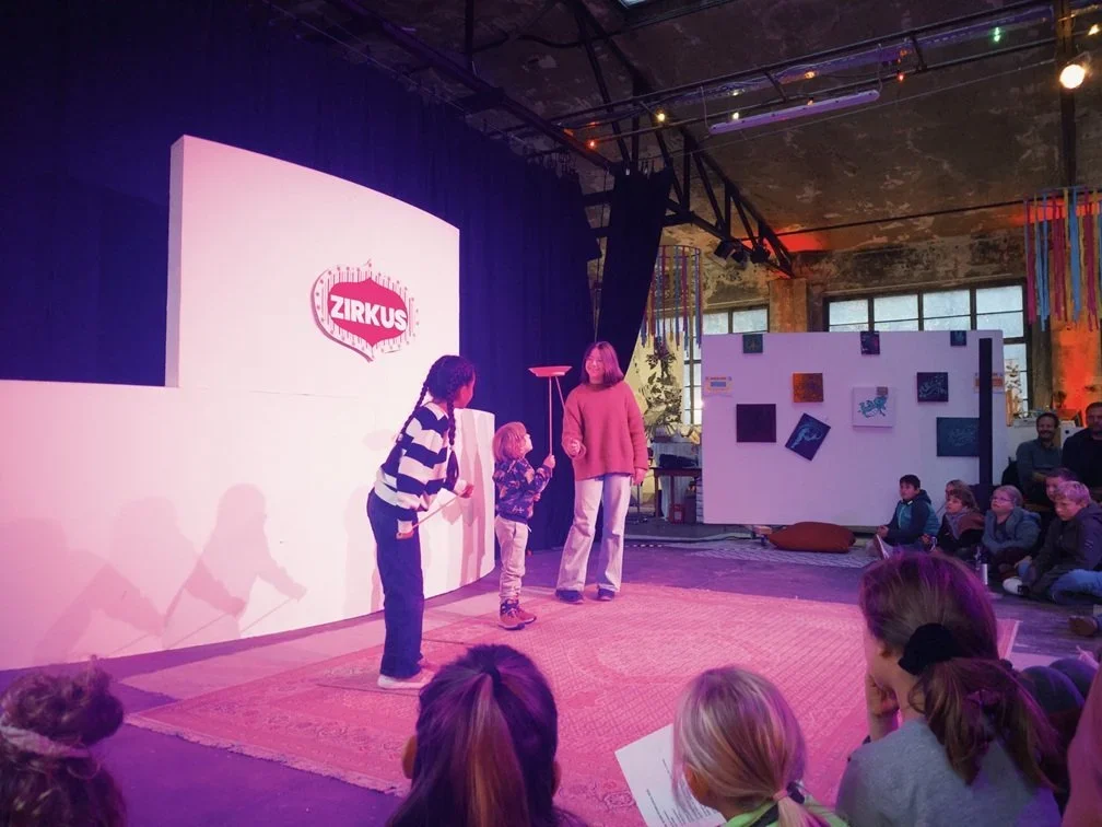 Drei Kinder präsentieren einen Tellertrick, im Hintergrund sieht man Teile der Ausstellung