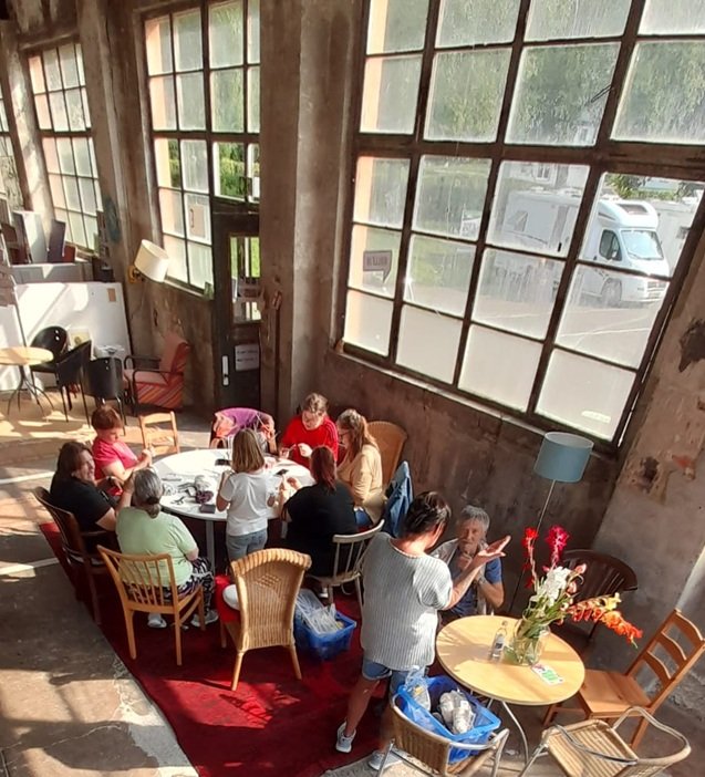 Teilnehmerinnen und Teilnehmer des Mittwochsangebotes beim künstlerischen Arbeiten. Es ist warm, die Türen sind offen und nebenher werden rege Gespräche geführt