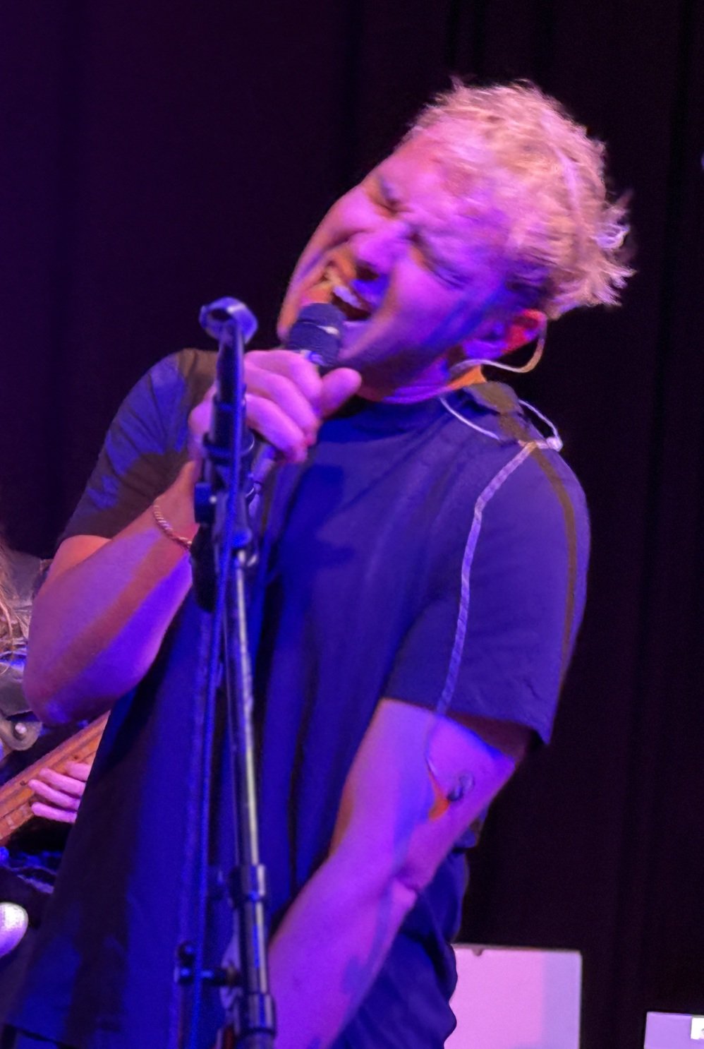 ein junger Mann mit blonden Haaren singt voller Emotionen mit einem Mikro in der Hand und weit aufgerissenem Mund