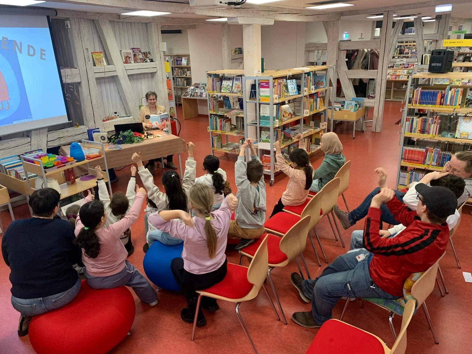 Die Kinder sitzen in der Bücherei und strecken ihre Daumen nach oben