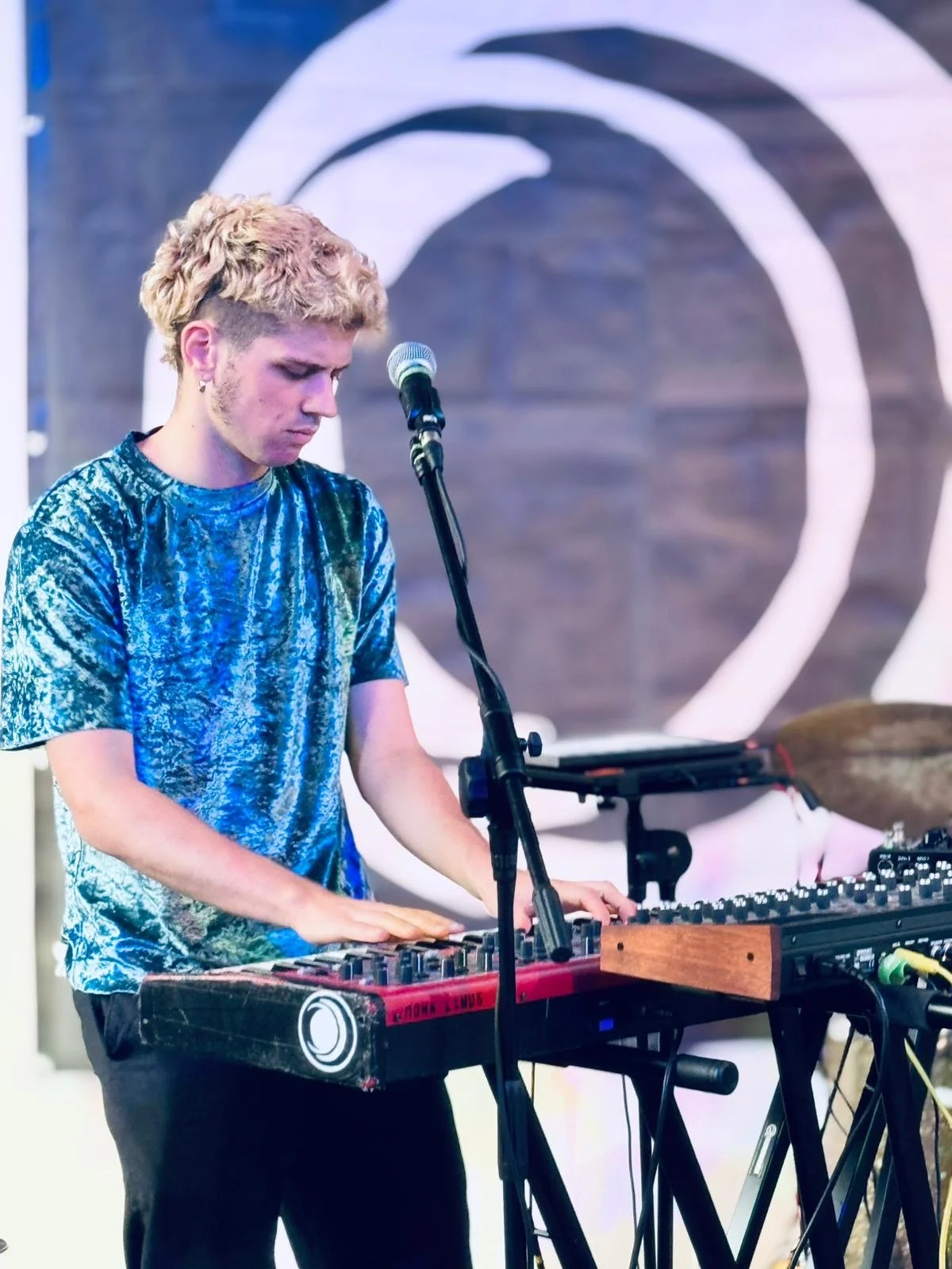 ein junger Mann mit hellblonden Haaren steht in einem hellblauen Oberteil am Keyboard und spielt