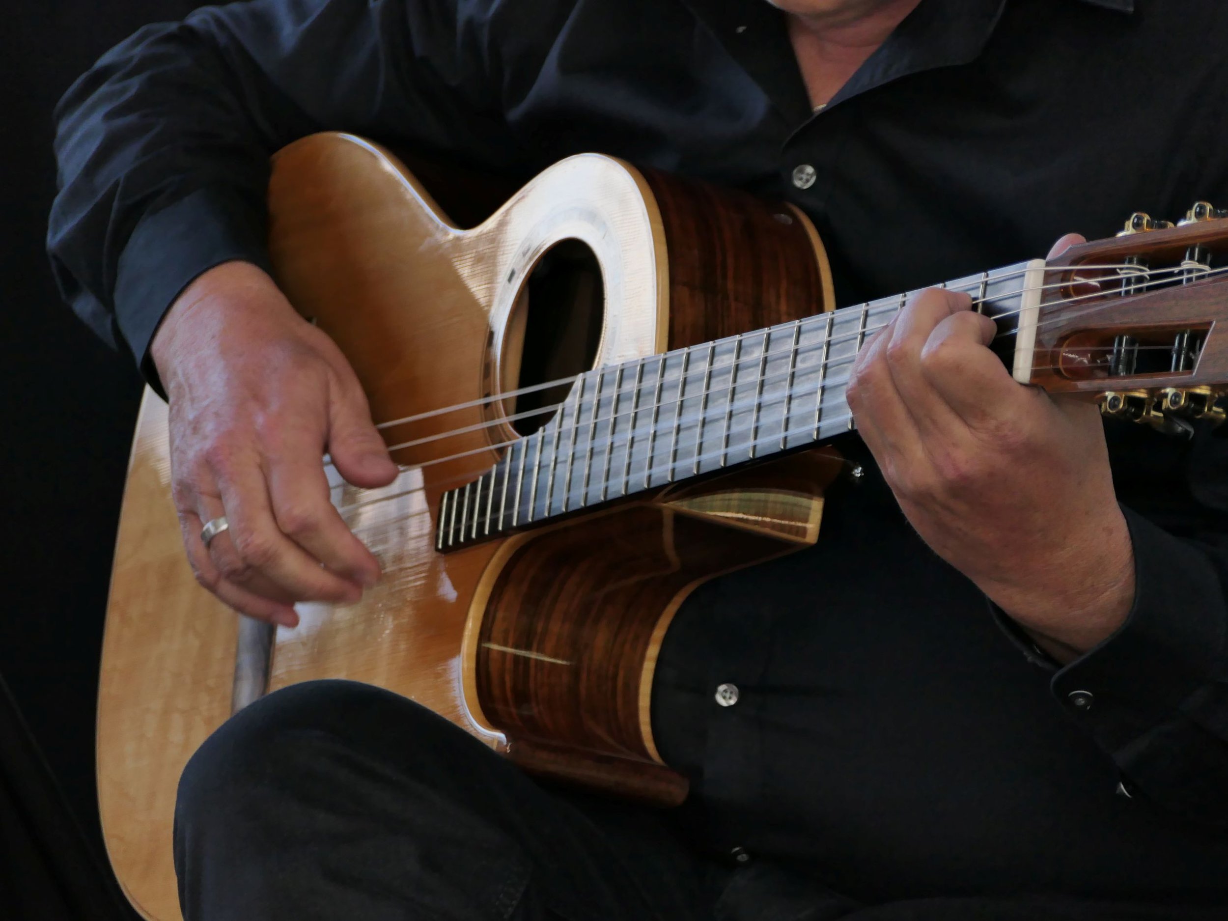 Nahaufnahme der besonderen Gitarre; Sie hat einen hölzernen Korpus, 6 Saiten, das Klangloch oberhalb der Saiten und ein Ausschnitt unten im Korpus, sodass möglichst weit hinten auf dem Hals gespielt werden kann.