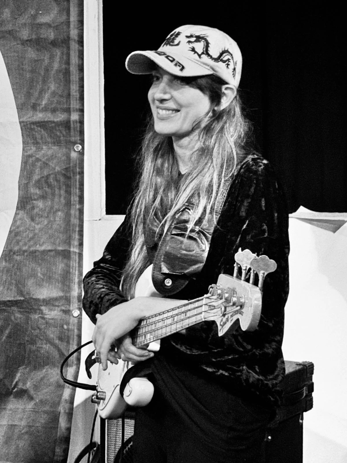 eine junge Frau mit langen Haaren und Cappie spielt Bass. Das Bild ist in schwarz-weiß