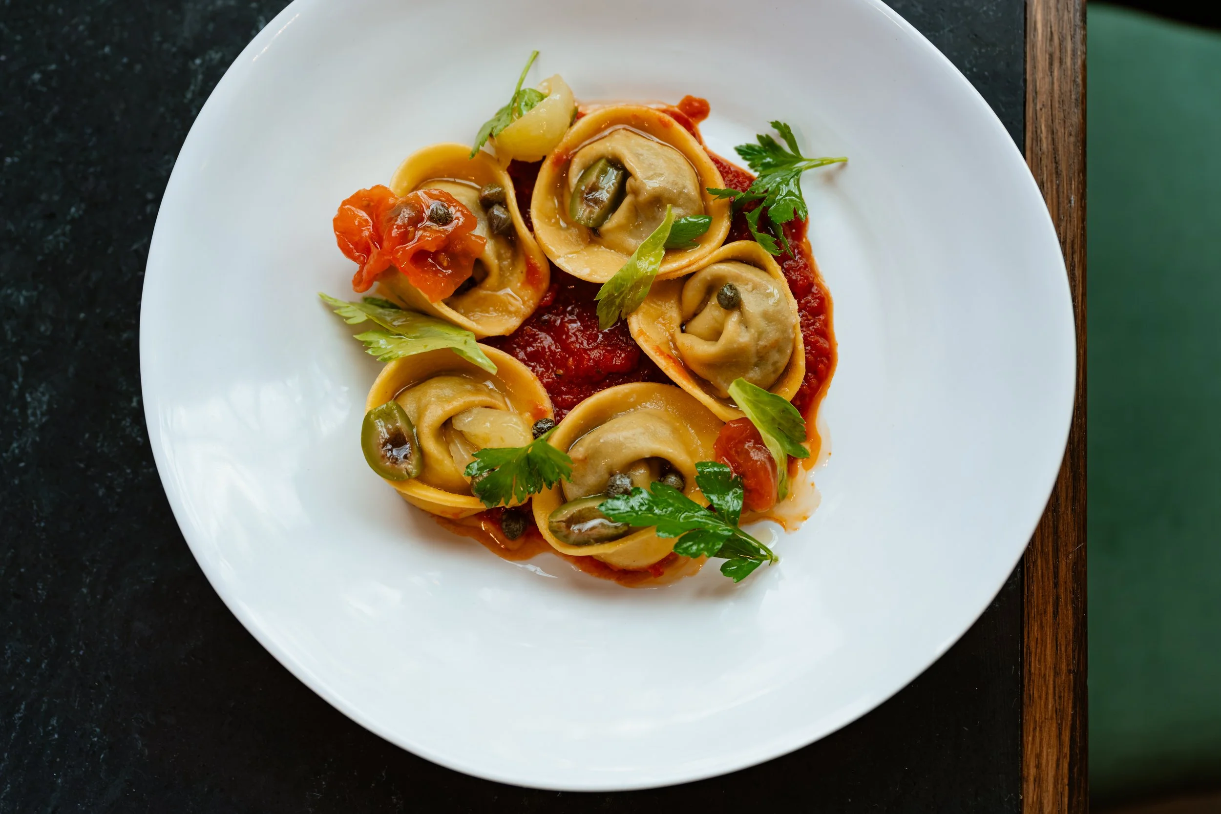 Plate of ravioli pasta with tomato sauce, garnished with fresh herbs and capers.