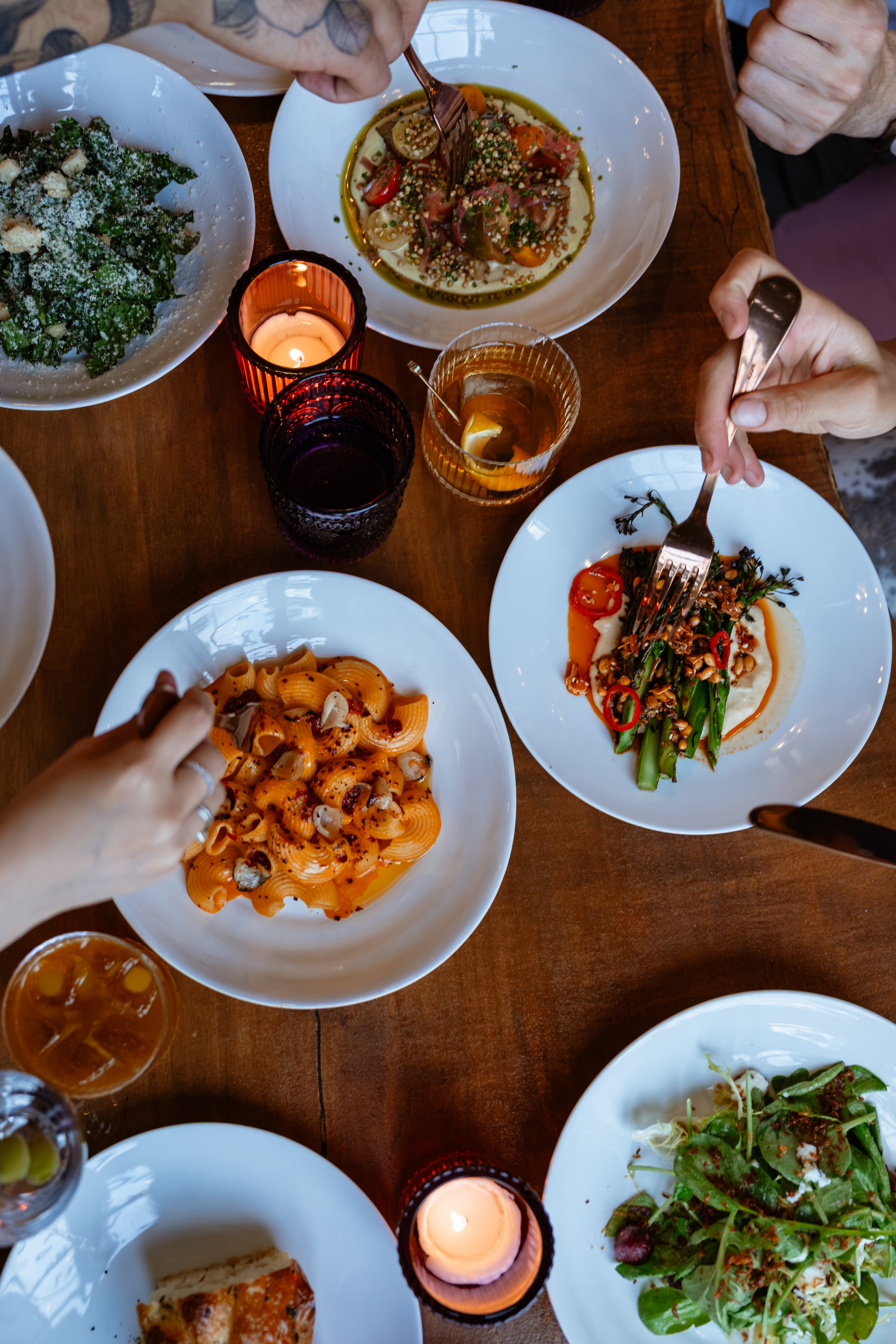 A top-down view of a dining table with various dishes, including a pasta, salad, and another entree, with candles and drinks.