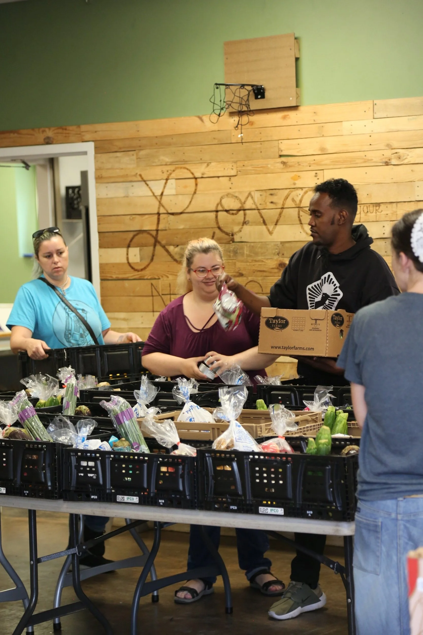 People organizing food items on a table, including bags of produce, in a community center.