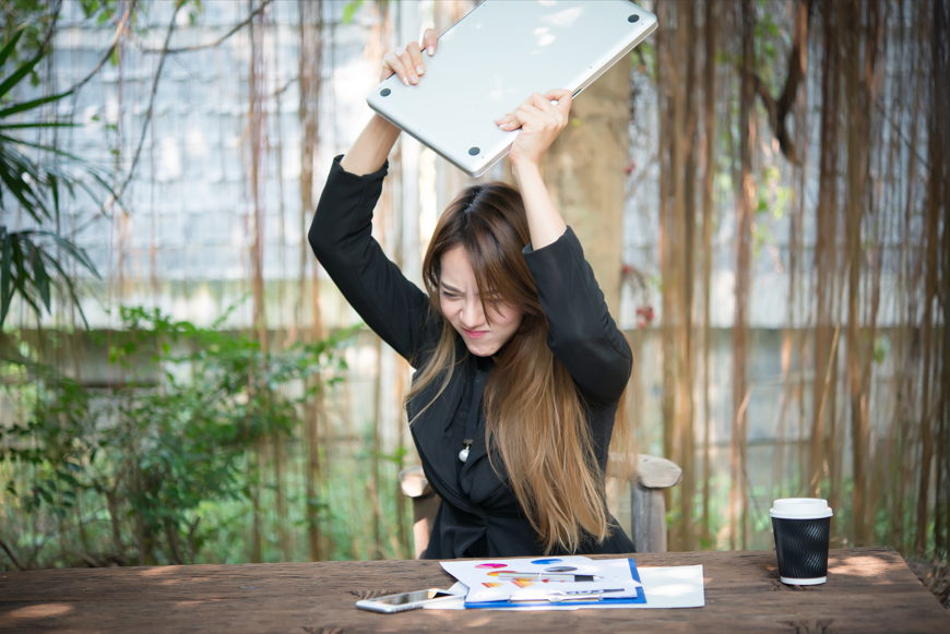 An angry woman raises a laptop over her head, expressing strong emotions and determination - Healing Family Addiction