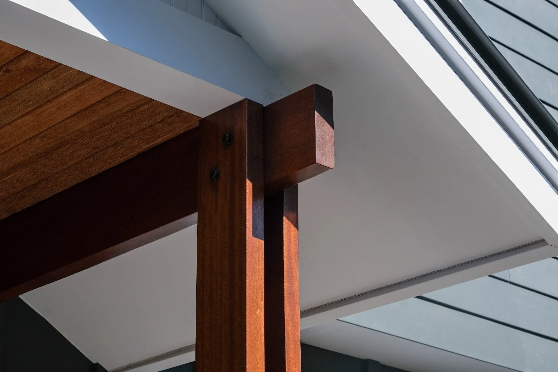 Close-up of wooden furniture joint with screws, situated near a skylight window with sunlight casting shadows.