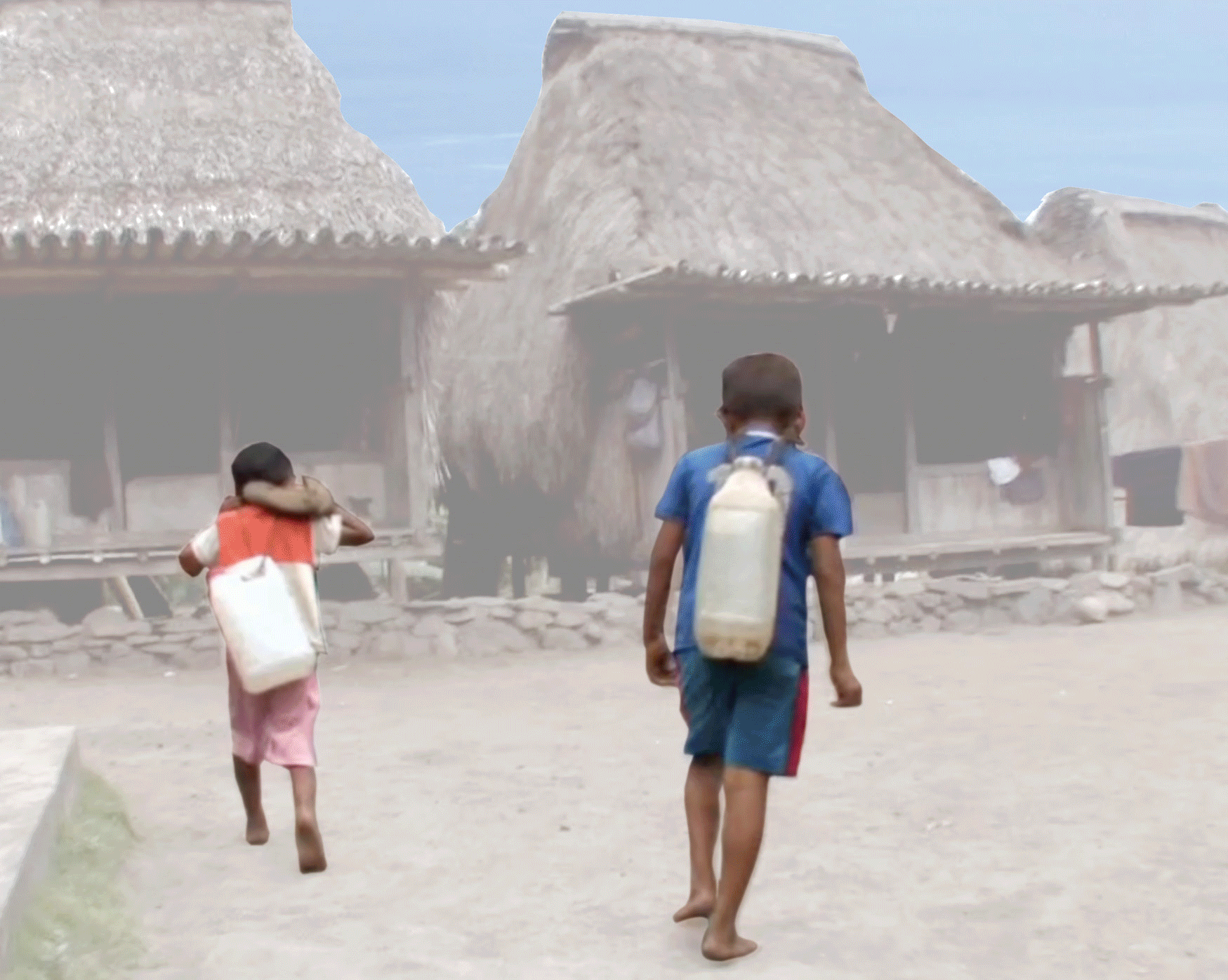 Two children walking on a dirt path in a rural village with thatched roof houses in the background.