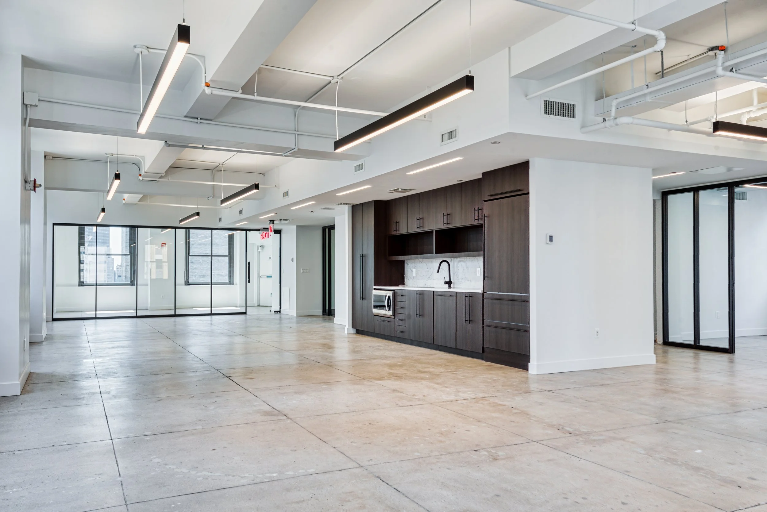 A full view of the office with concrete floors, a Pantry, and glass front offices