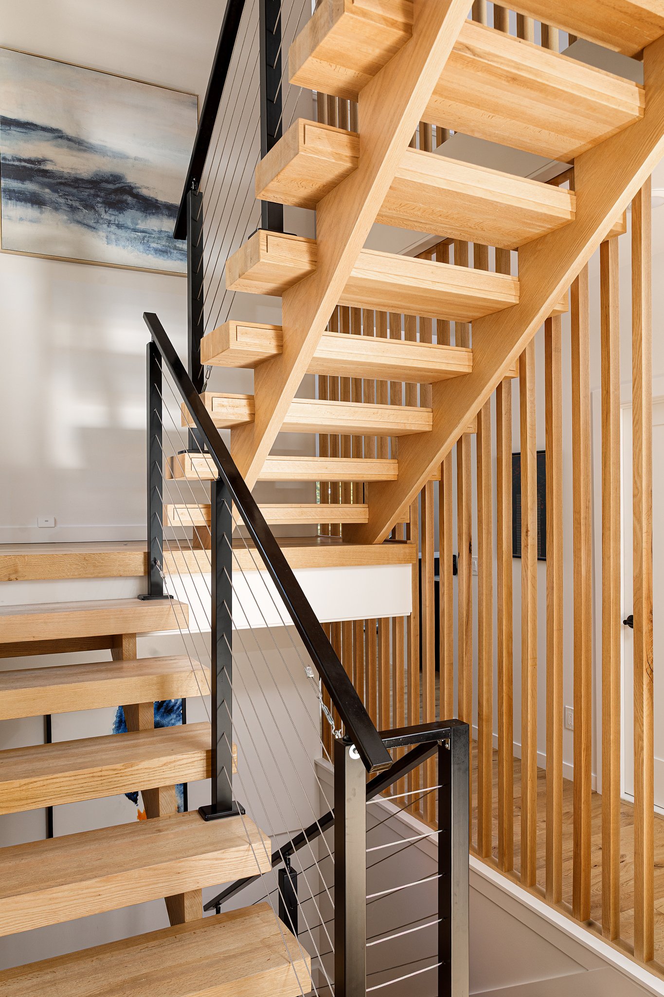 A modern wooden staircase with black metal railing and vertical wooden slats on the side, located inside a contemporary home.