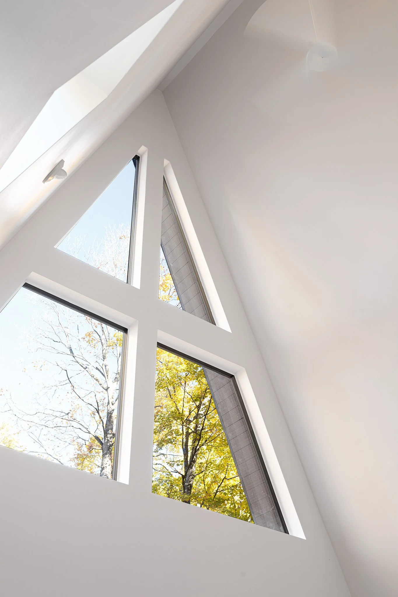 Interior view of large, triangular windows with autumn-colored trees outside.