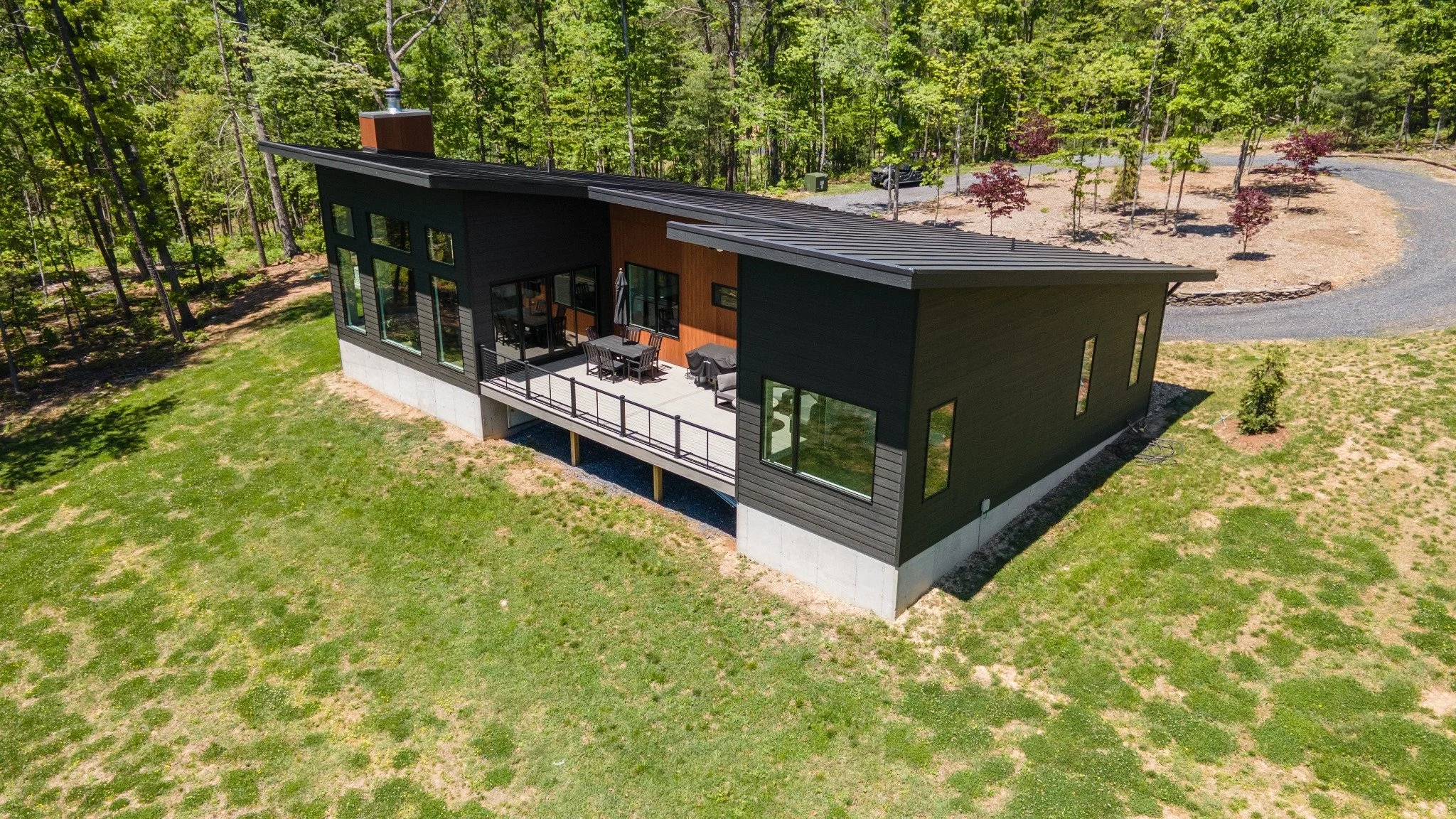 Mountain house architect project featuring dark siding, a sloping metal roof, tall windows, and a raised dining deck seen from the air.
