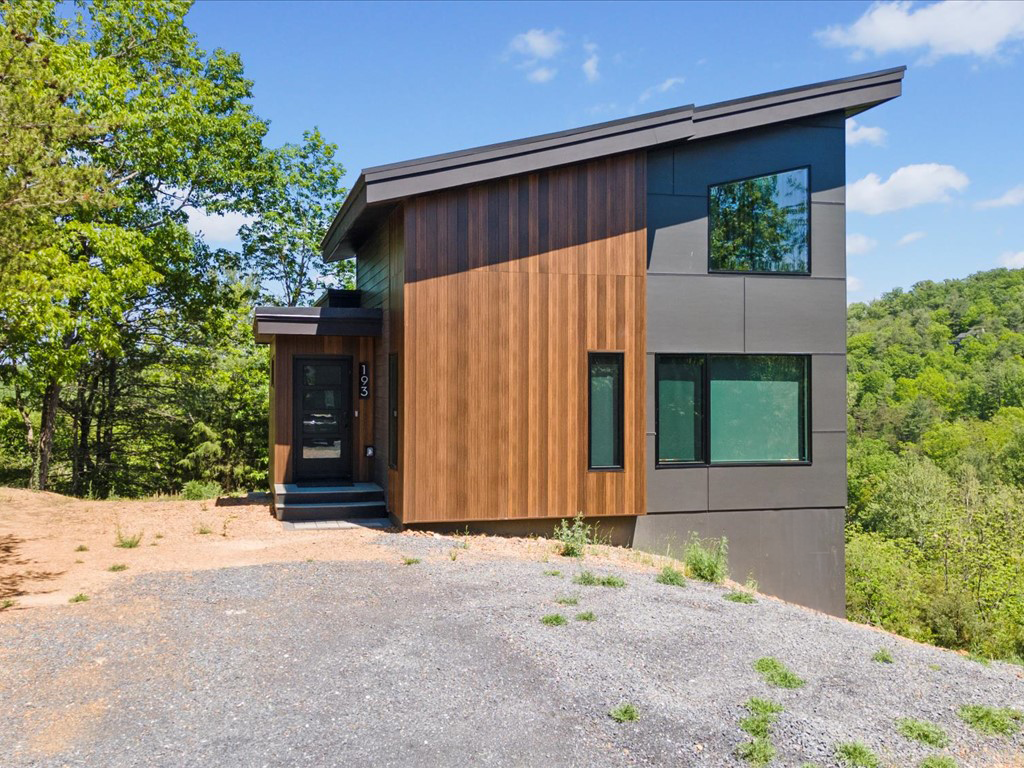 Residential architect project featuring vertical wood siding, gray exterior panels, a sloping roof, and an entry beside a gravel driveway.
