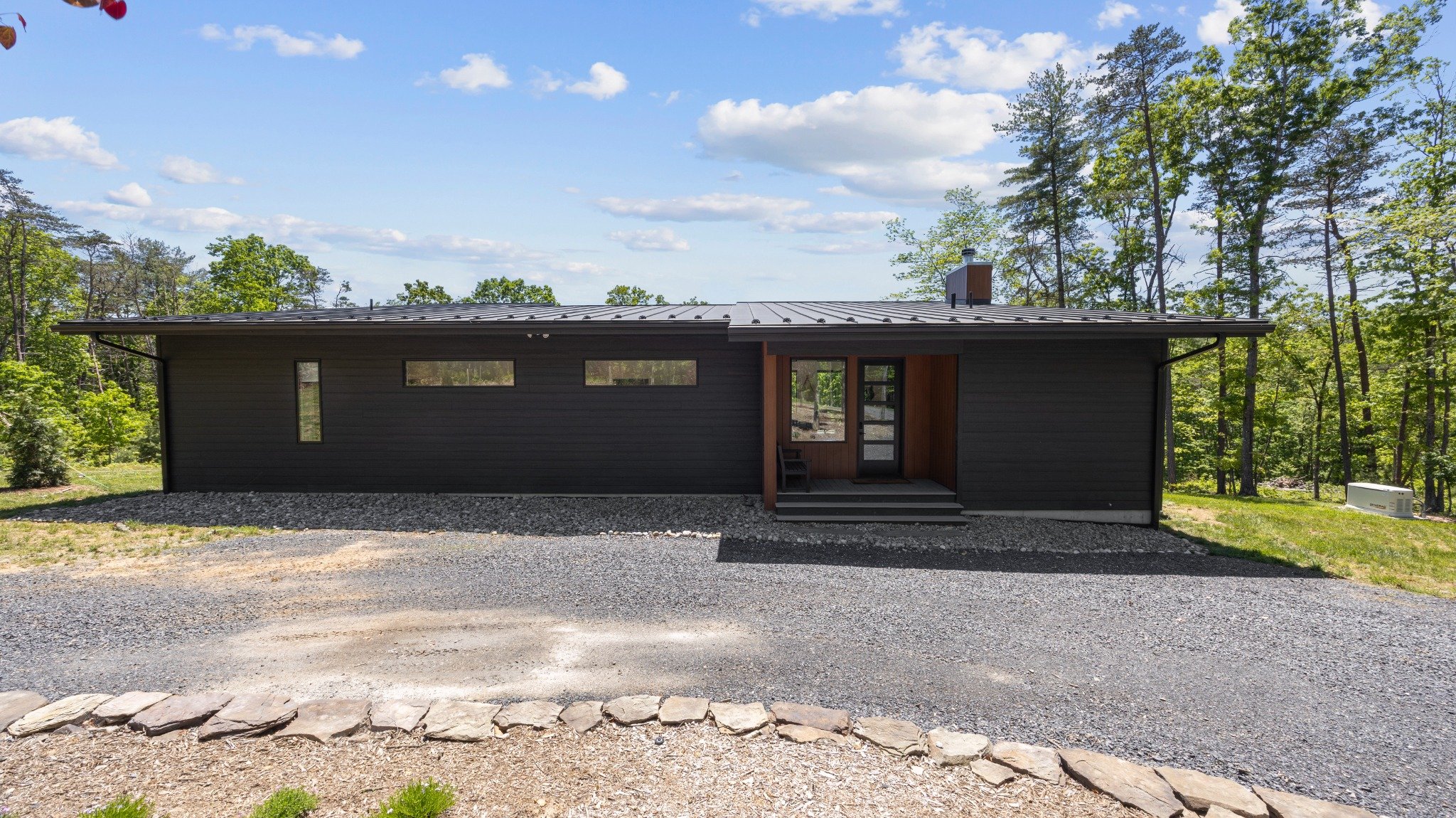 Modern mountain home architect project featuring dark horizontal siding, narrow windows, a wood-lined entry, and a low metal roof.