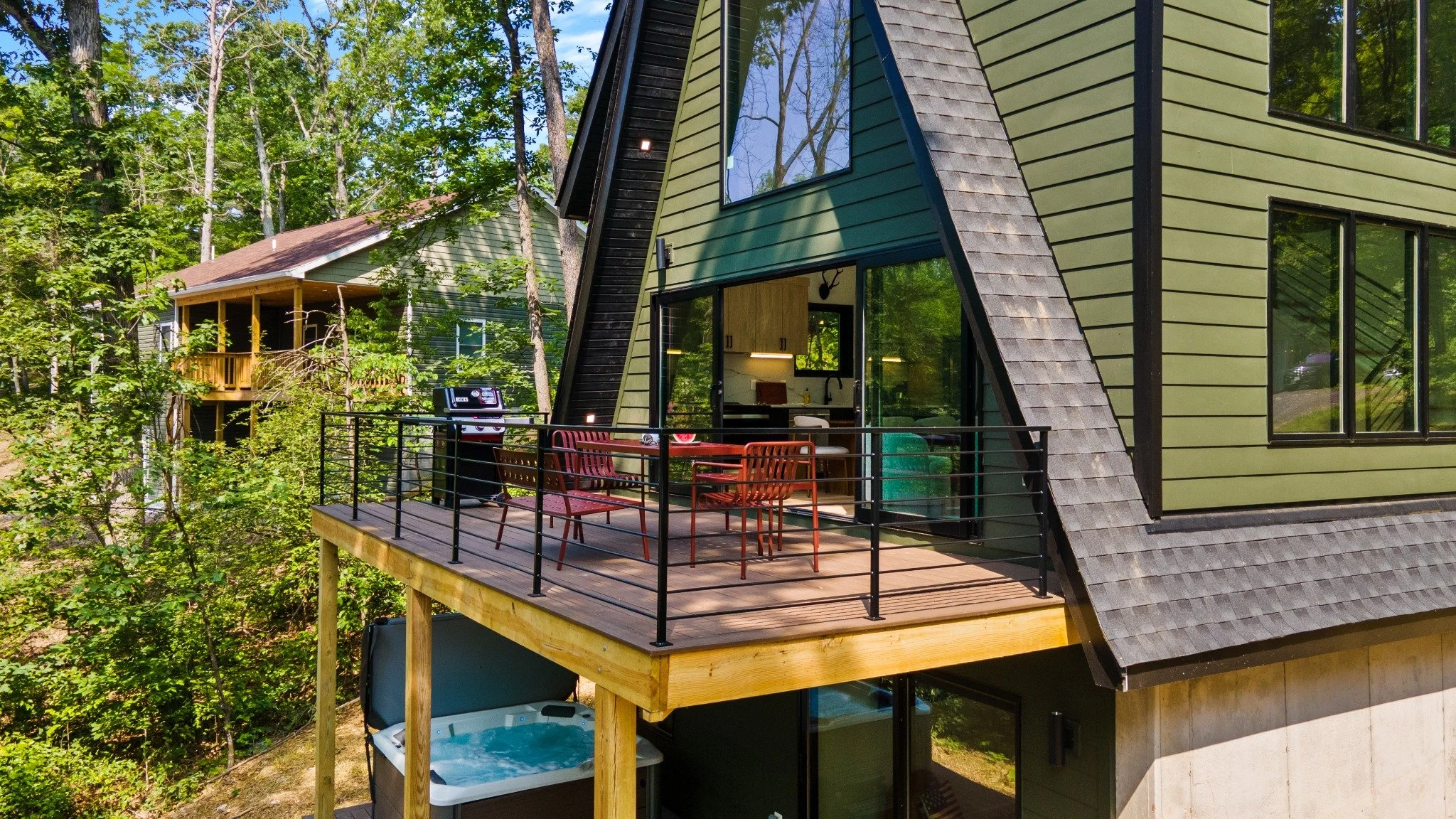 Mountain home architect project featuring a raised wood deck, red dining furniture, black railings, and a sheltered hot tub below.