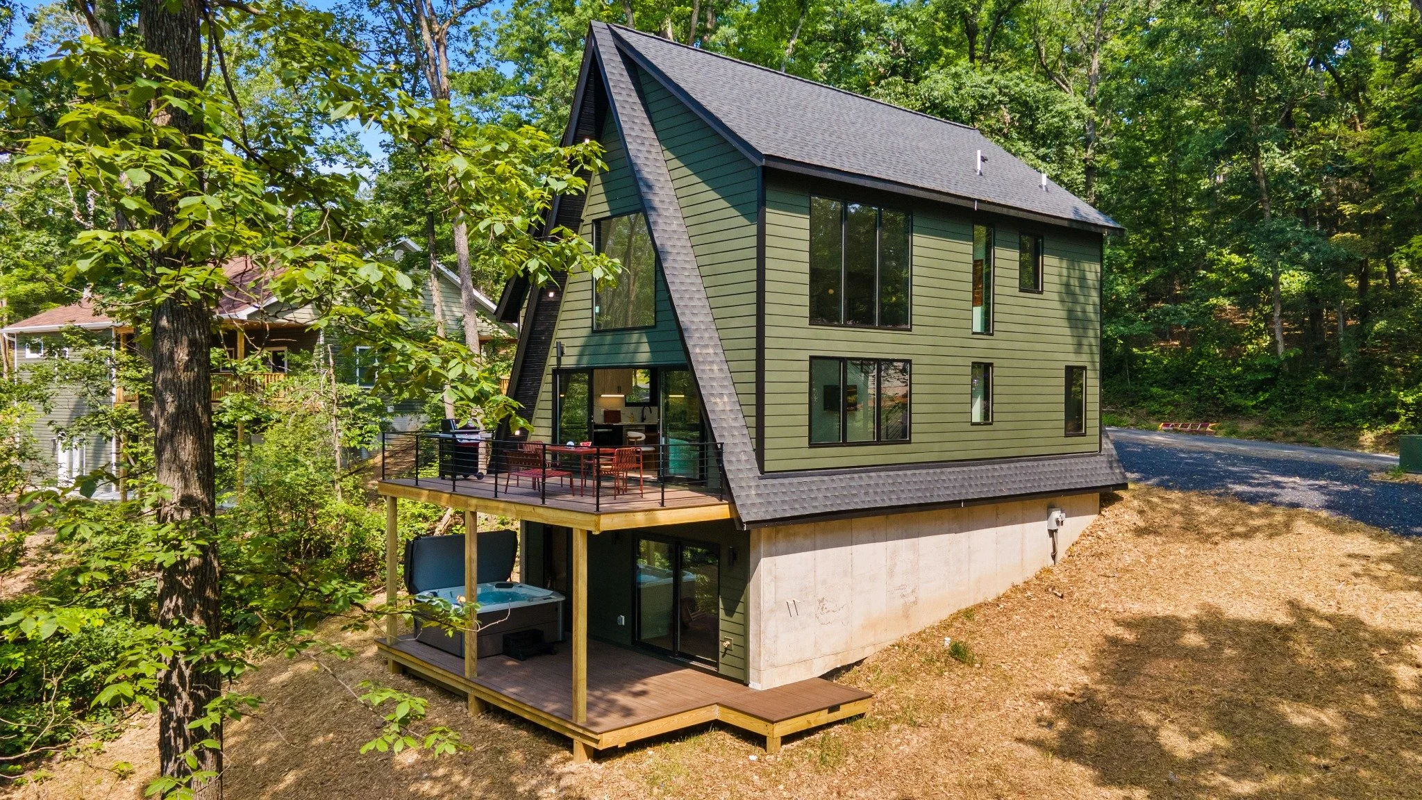 Custom home designer project featuring green siding, a steep roof, an upper dining deck, and a hot tub on the lower deck.