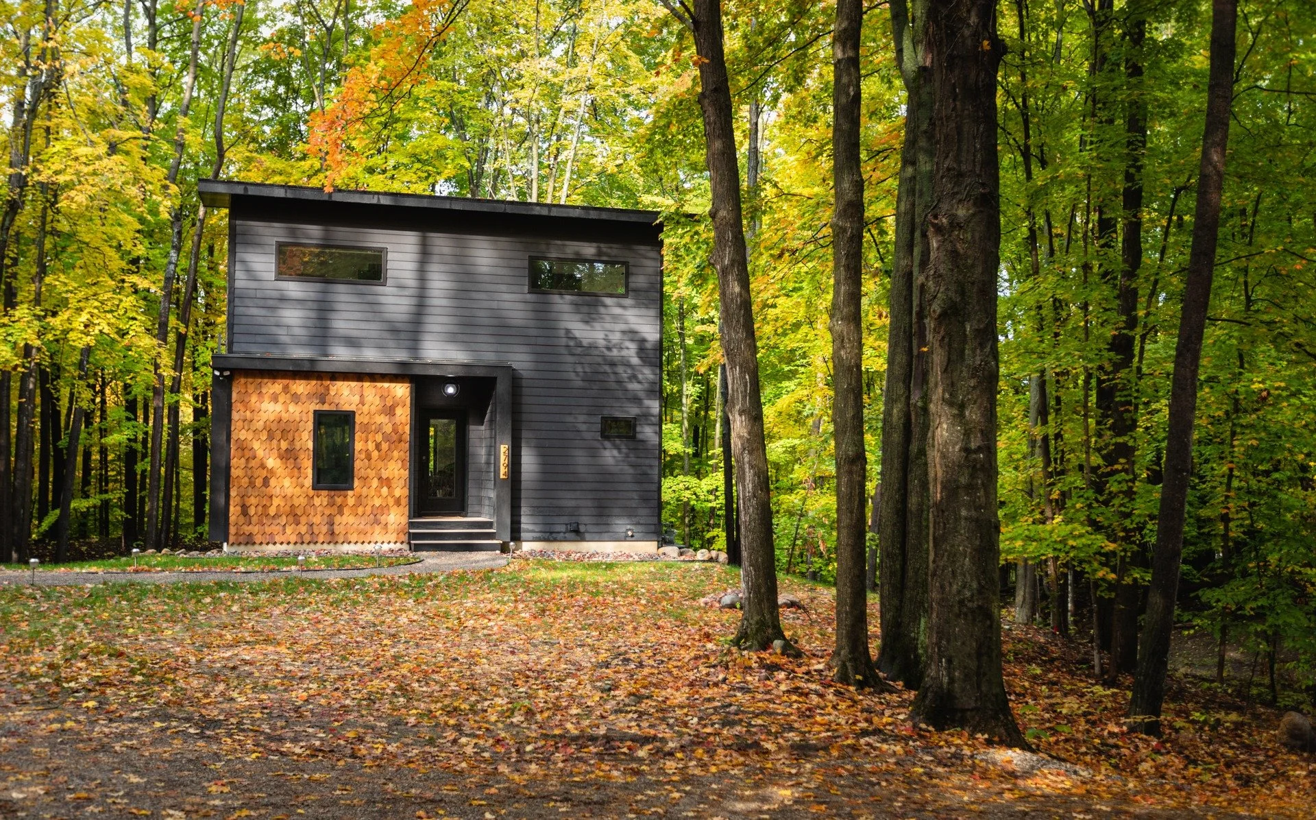 Custom mountain home architect project featuring dark horizontal siding, a wood-shingle entry accent, and a recessed front door among autumn trees