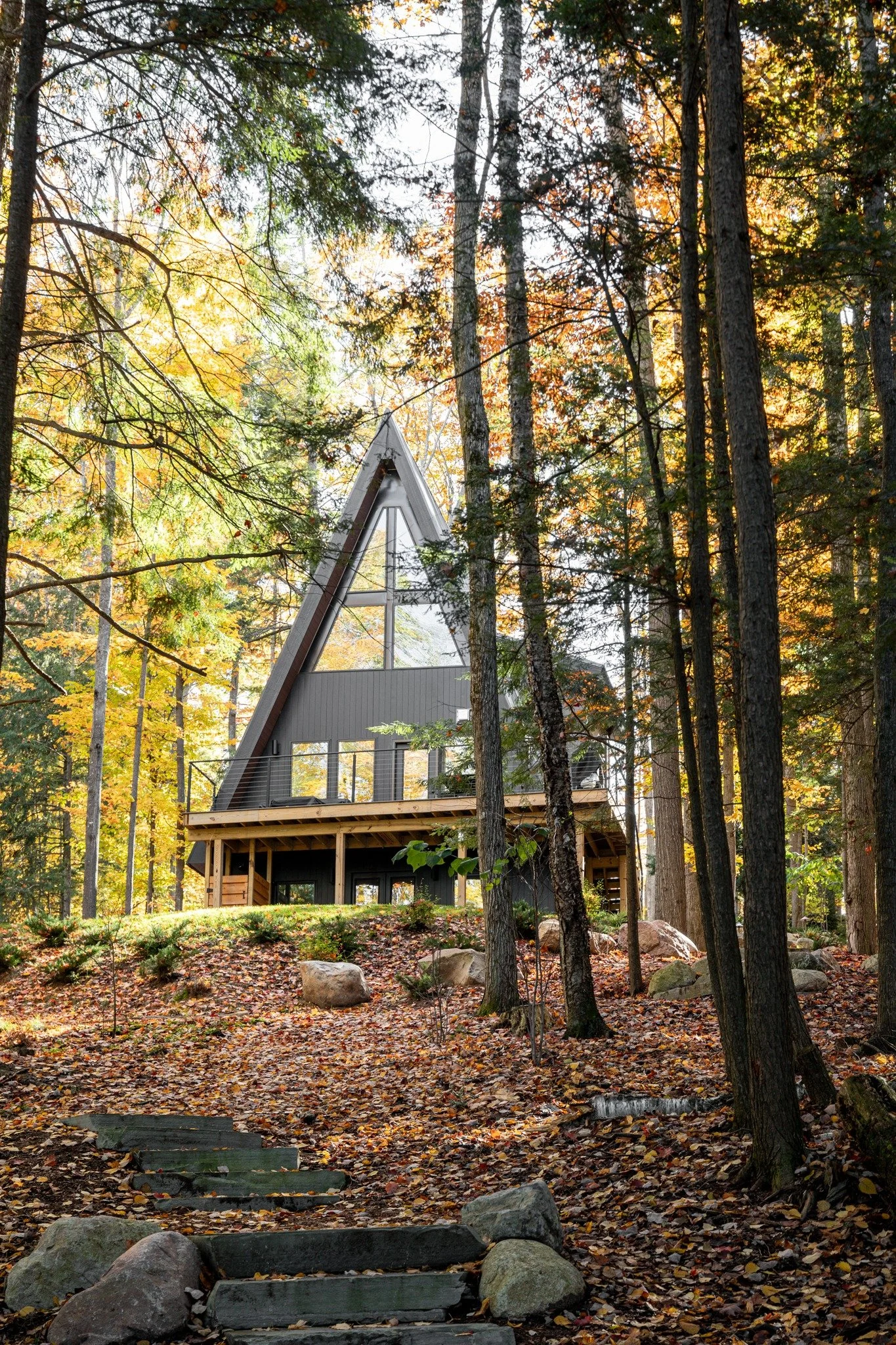 Custom lakefront home design with an A-frame roof, an upper balcony, a circular window, and a lower dining deck.
