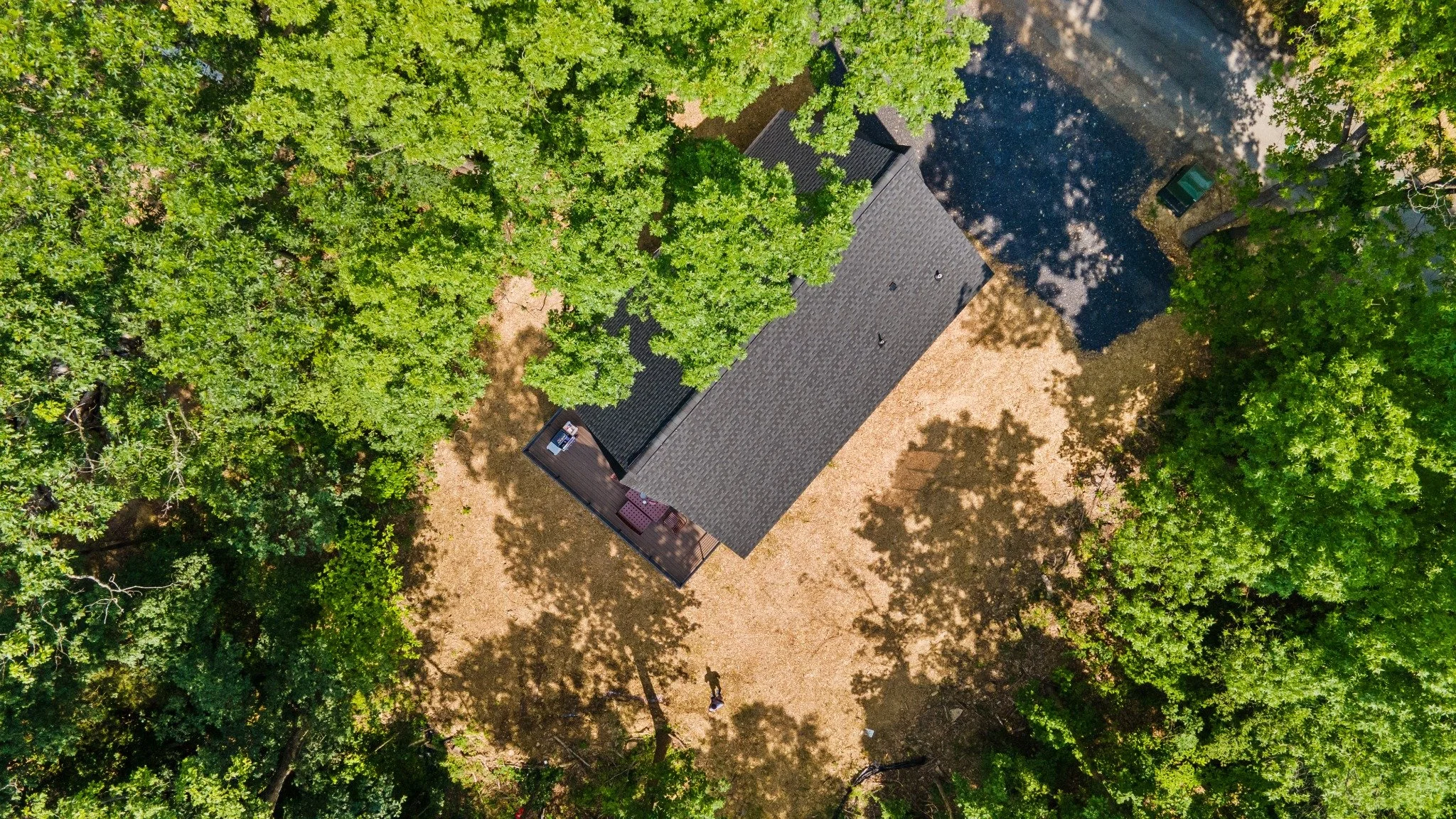 Modern mountain home architect project featuring an overhead view of a steep shingle roof, an outdoor deck, and a gravel driveway among trees.