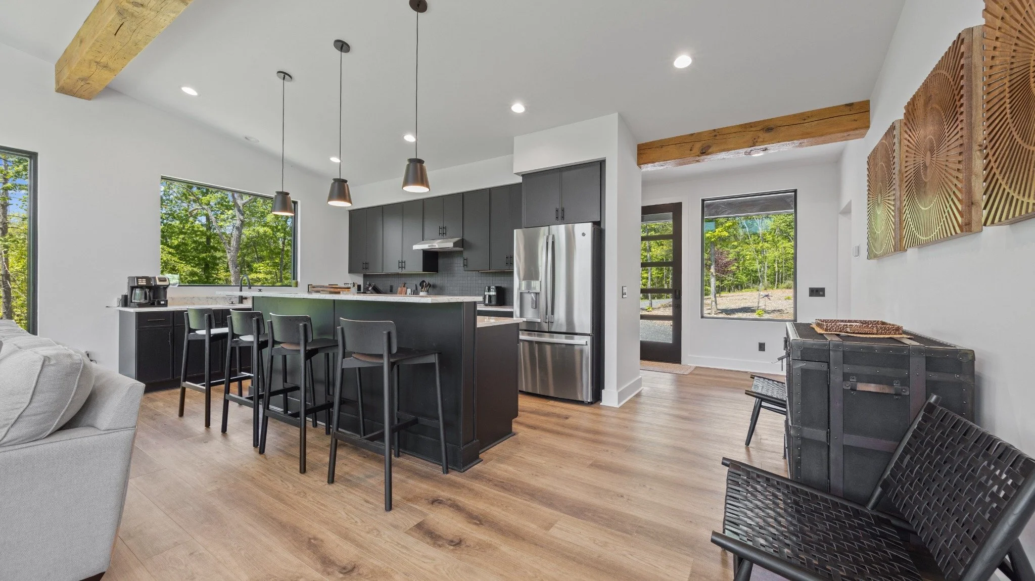 Mountain home designer project featuring dark cabinets, a large island, black stools, pendant lights, and exposed wood beams.