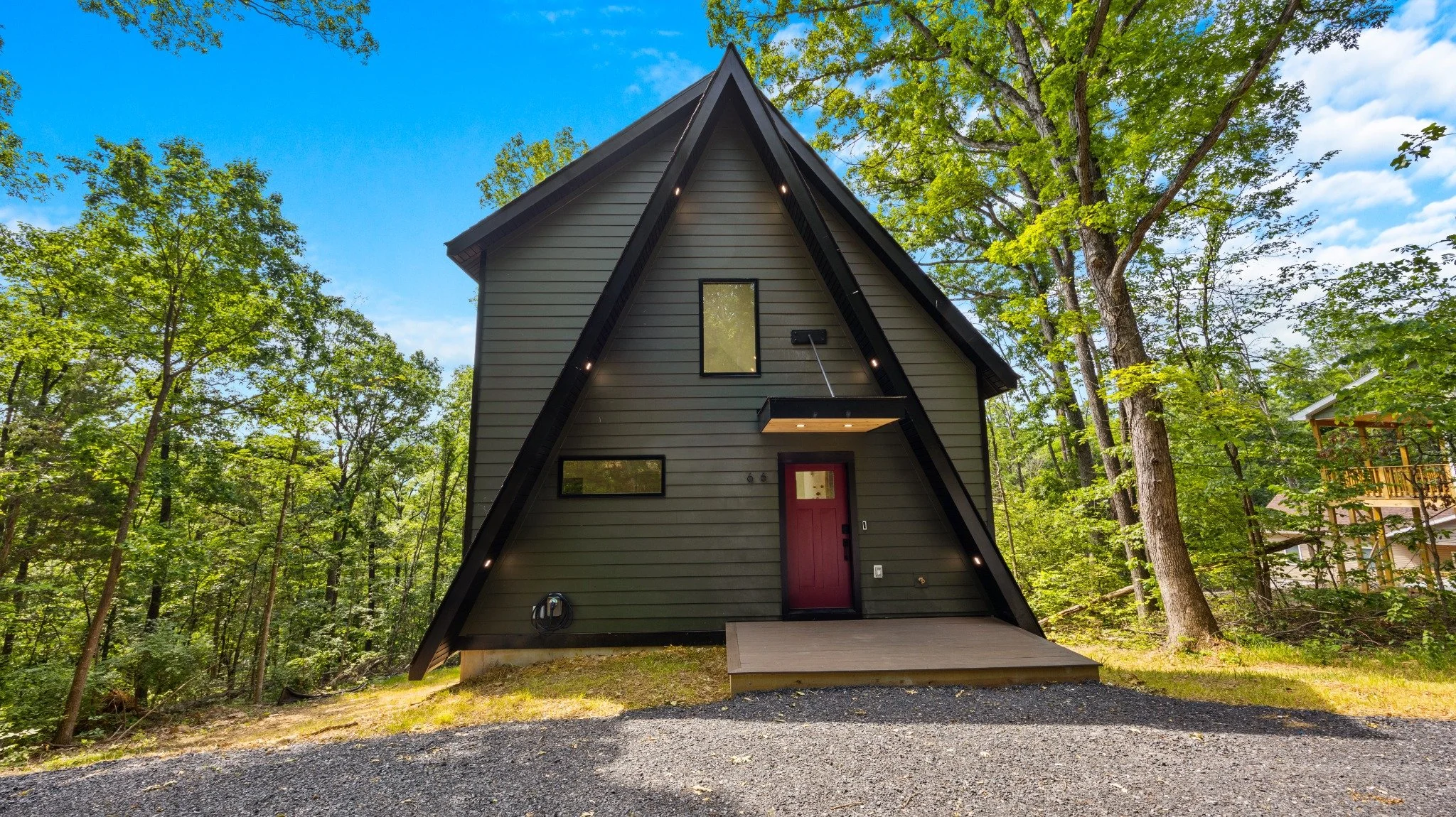 Custom mountain home designer project featuring an A-frame roof, green siding, a red entry door, and a small entry deck among trees.