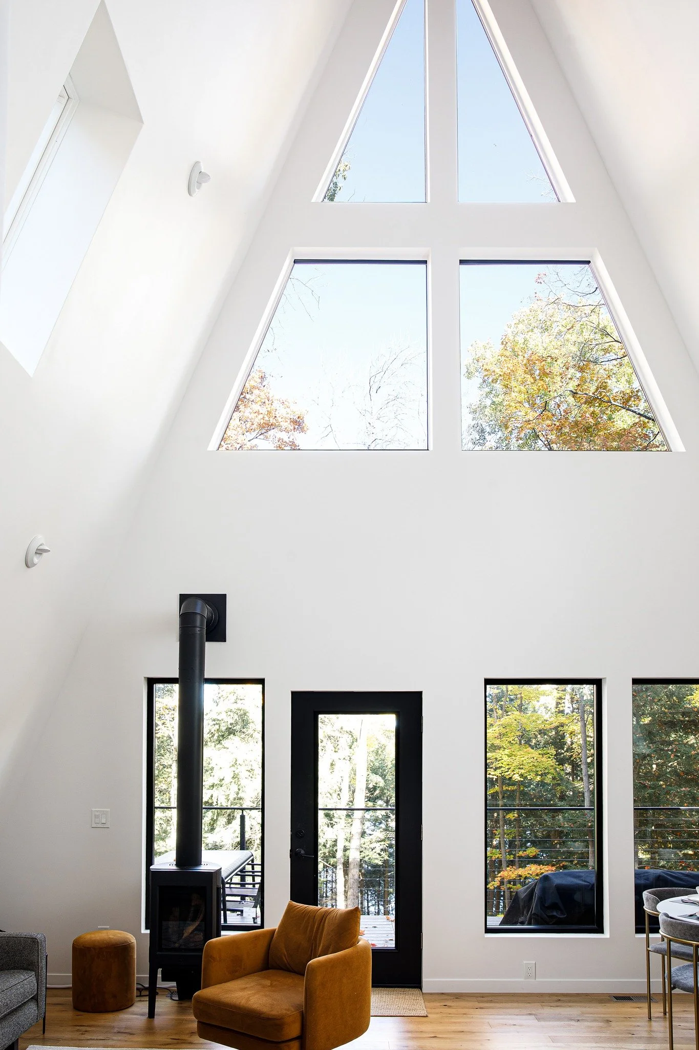 Modern lake house interiors with a steep white ceiling and triangular windows framing blue sky and autumn trees.