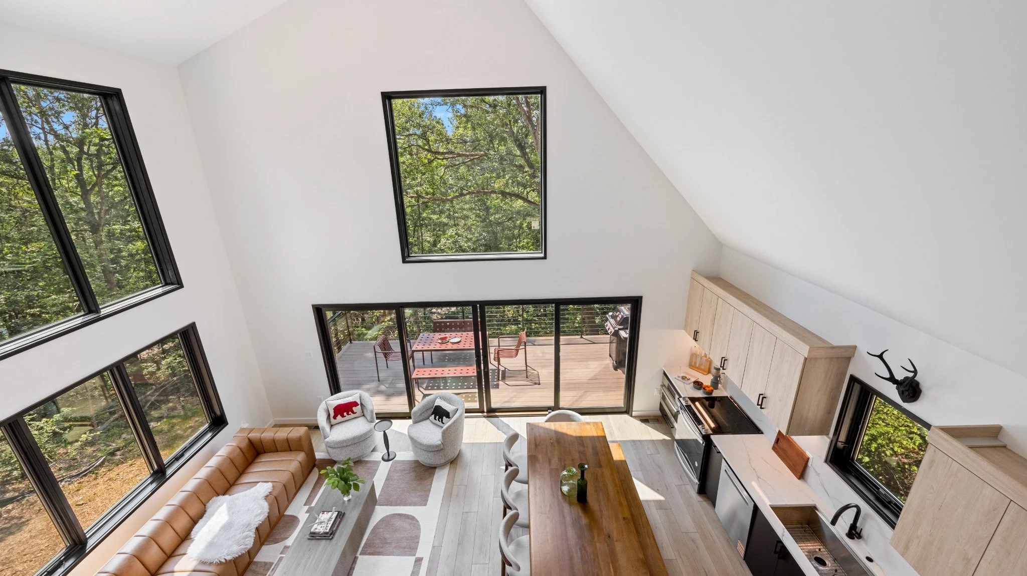 Modern mountain home architect project featuring a loft view of a double-height living area, open kitchen, wood dining table, and doors to a deck.