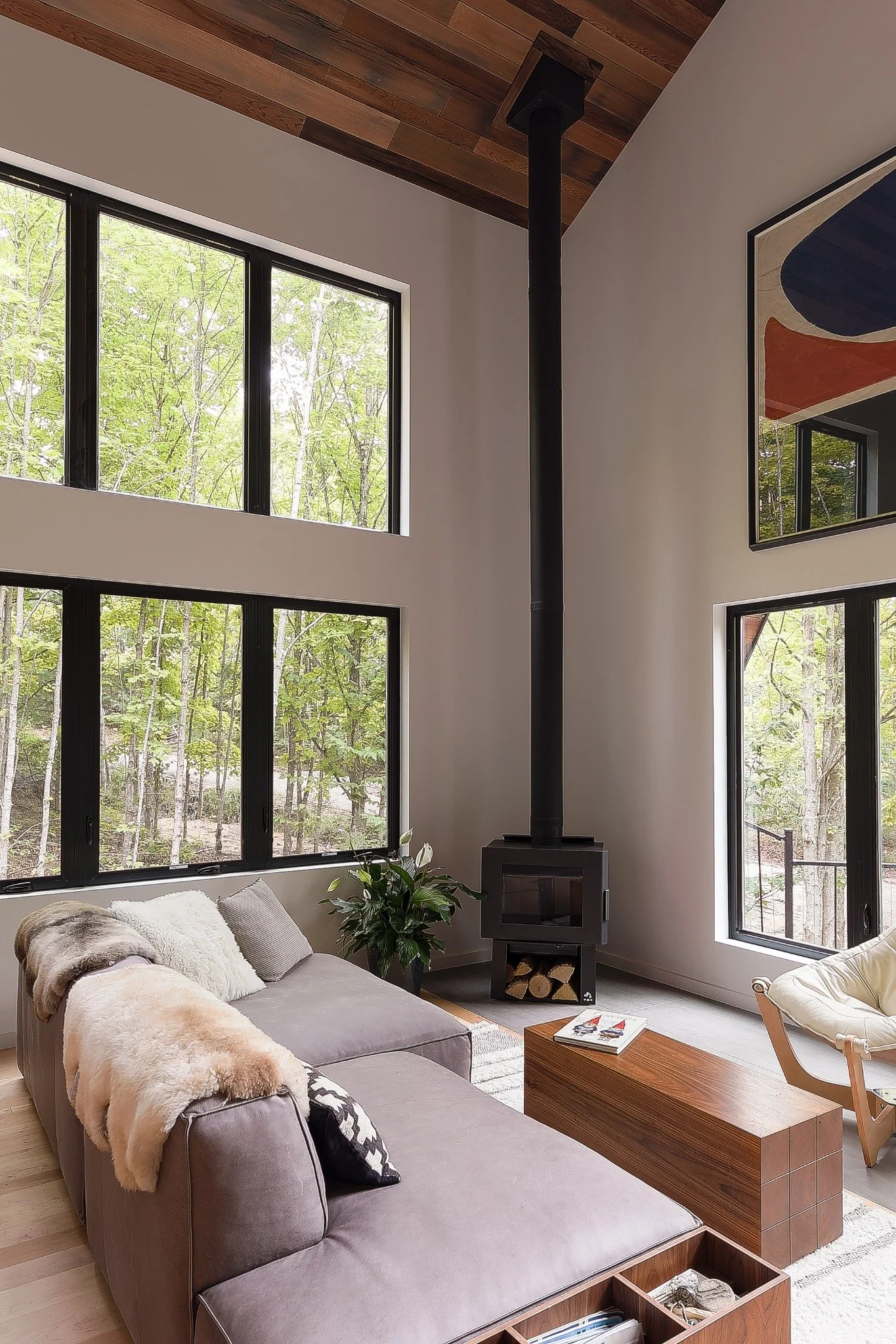 Lake house design with a high white ceiling, triangular windows, a black wood stove, and a mustard-colored lounge chair.
