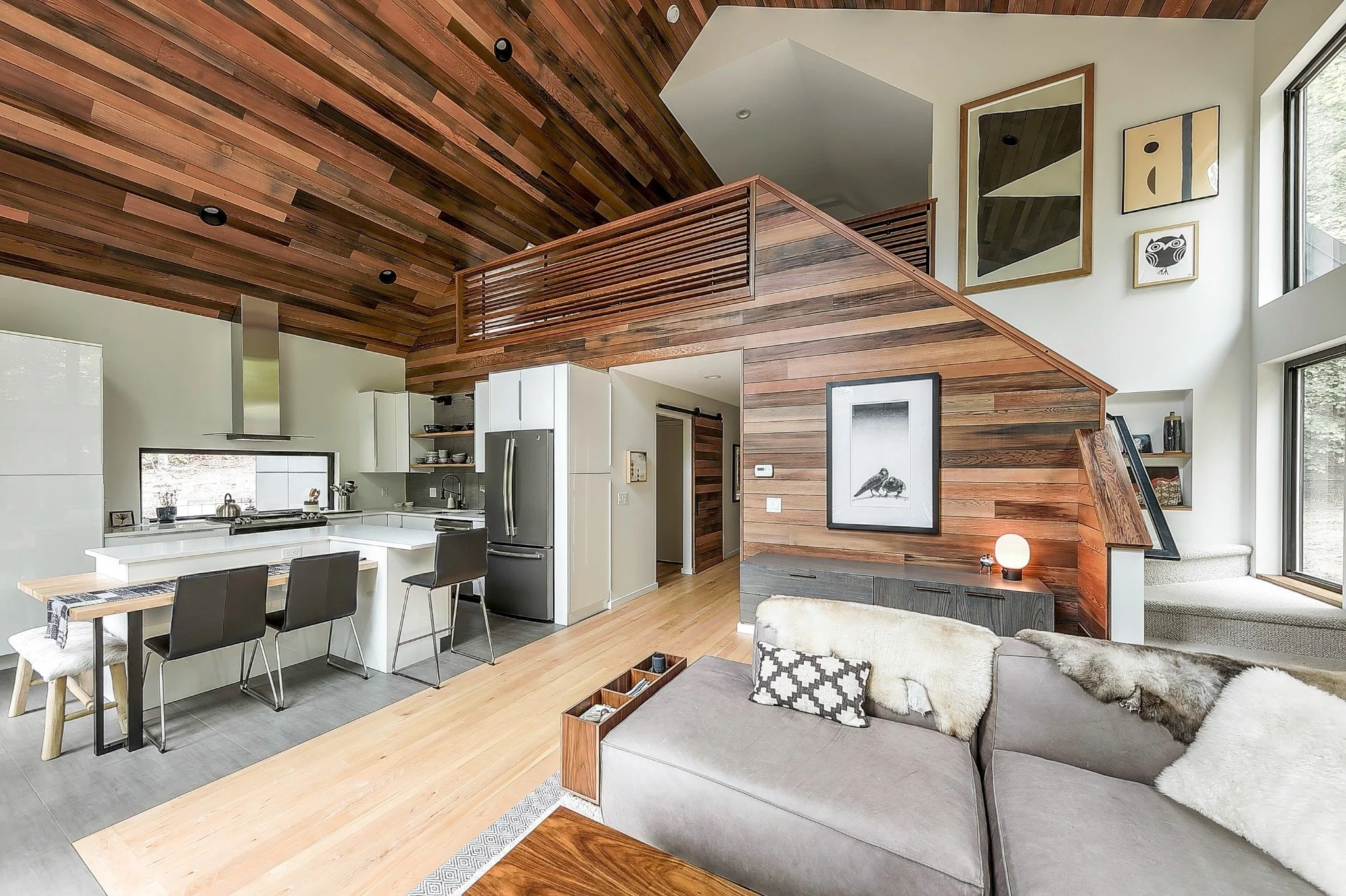 Custom waterfront home design with an open kitchen and living area, white cabinetry, wood-lined ceiling, and loft above.
