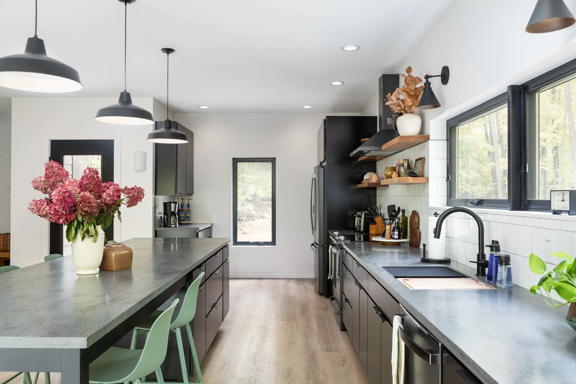 Mountain home designer project featuring black cabinetry, gray countertops, green island stools, wood shelves, and black pendant lights.