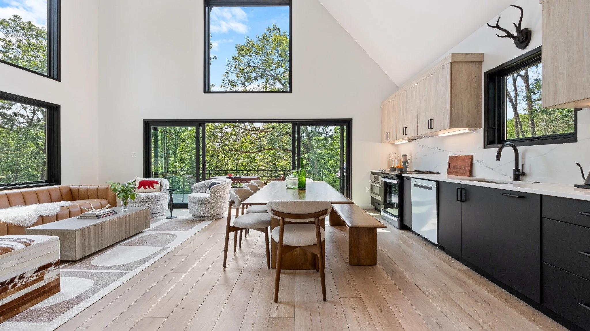 Custom mountain home designer project featuring wood upper cabinets, dark lower cabinets, a wood dining table, and an open living area beside glass doors.