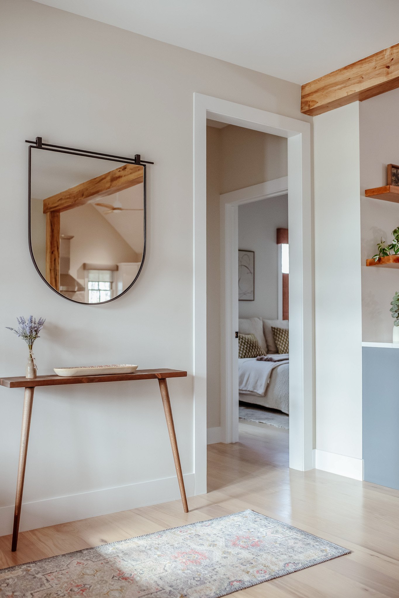 Minimalist interior decor with a white vase holding flowering branches, a modern white lamp with a round base, a wooden decorative object, and small black bowls on a white surface near a window.