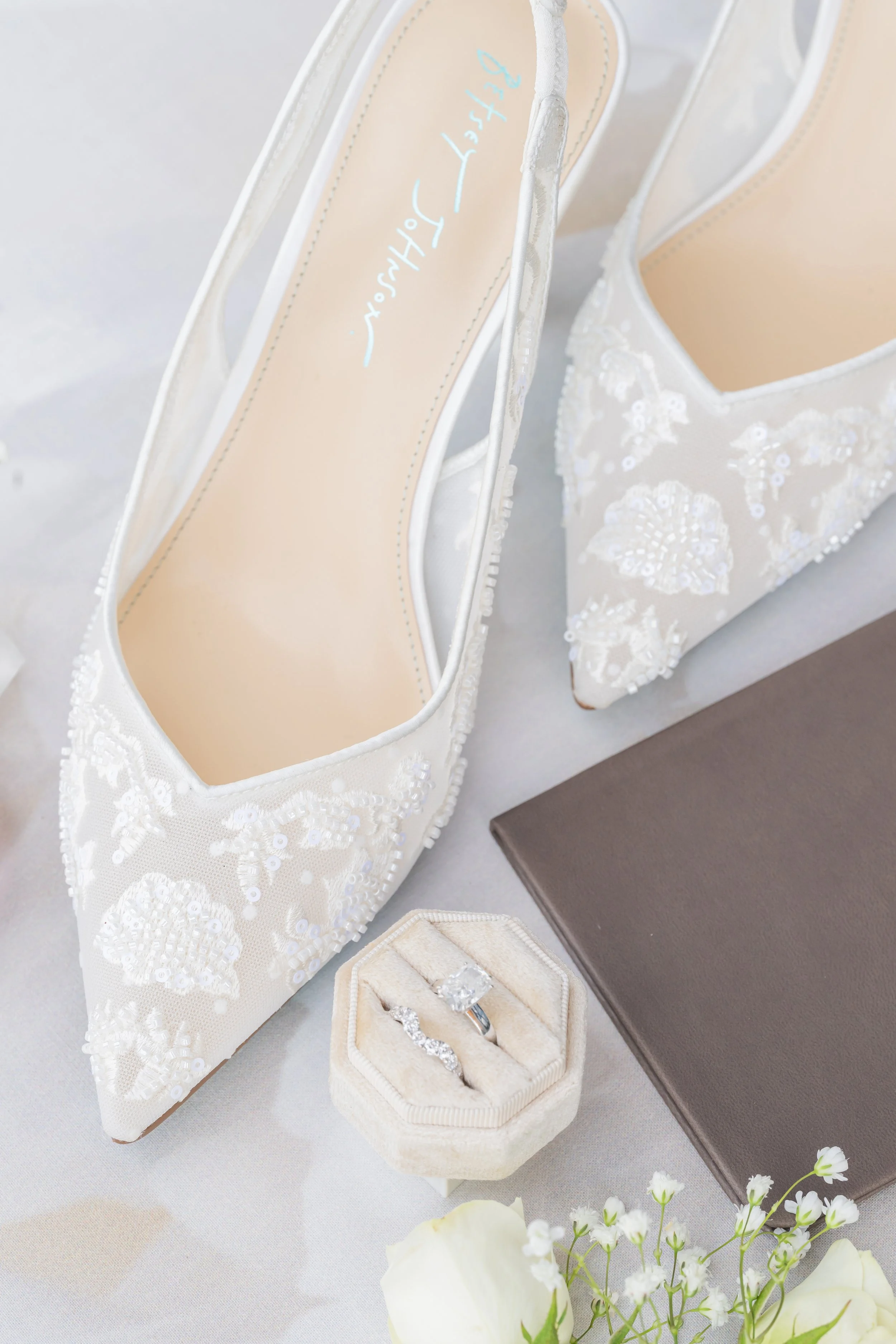 Details shot of bride's shoes, wedding rings, and vow book
