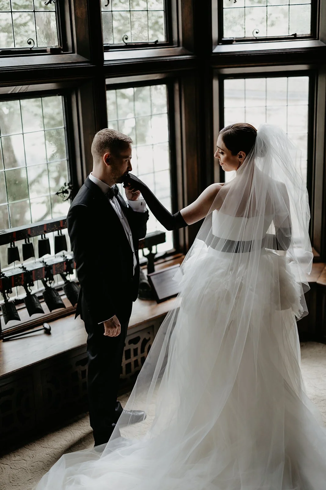 Groom kisses bride's hand by a window