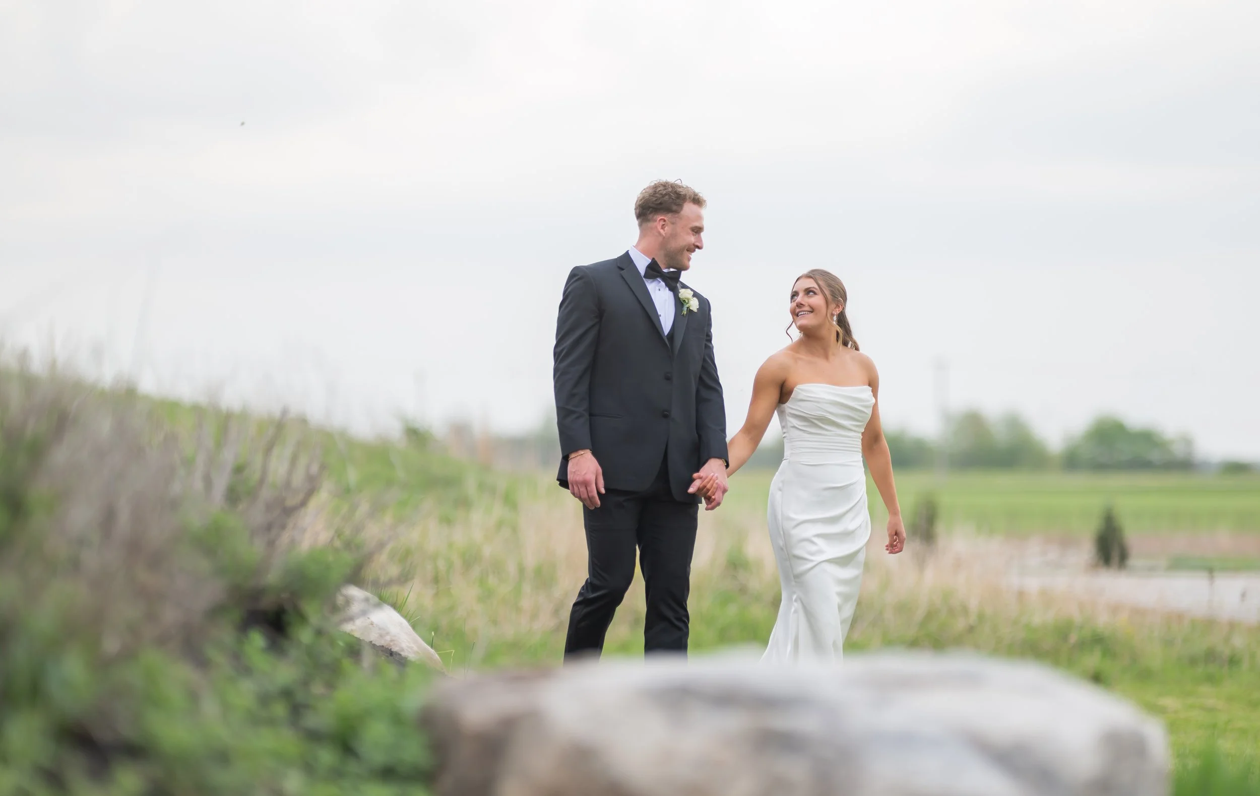 Portrait of a bride and groom smiling at each other as they walk through a field