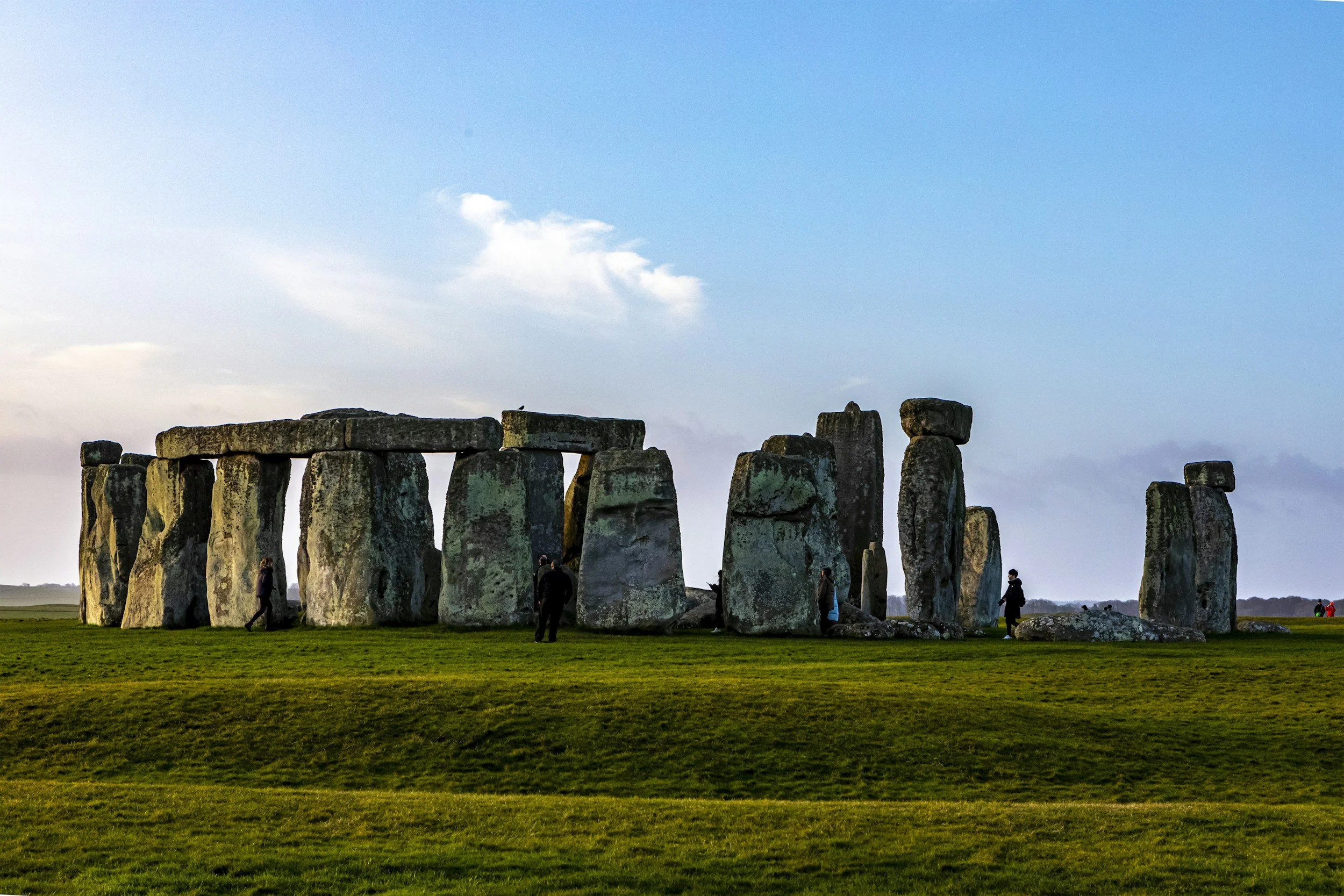 Stonehenge monument with a few visitors, under a partly cloudy sky during daytime.