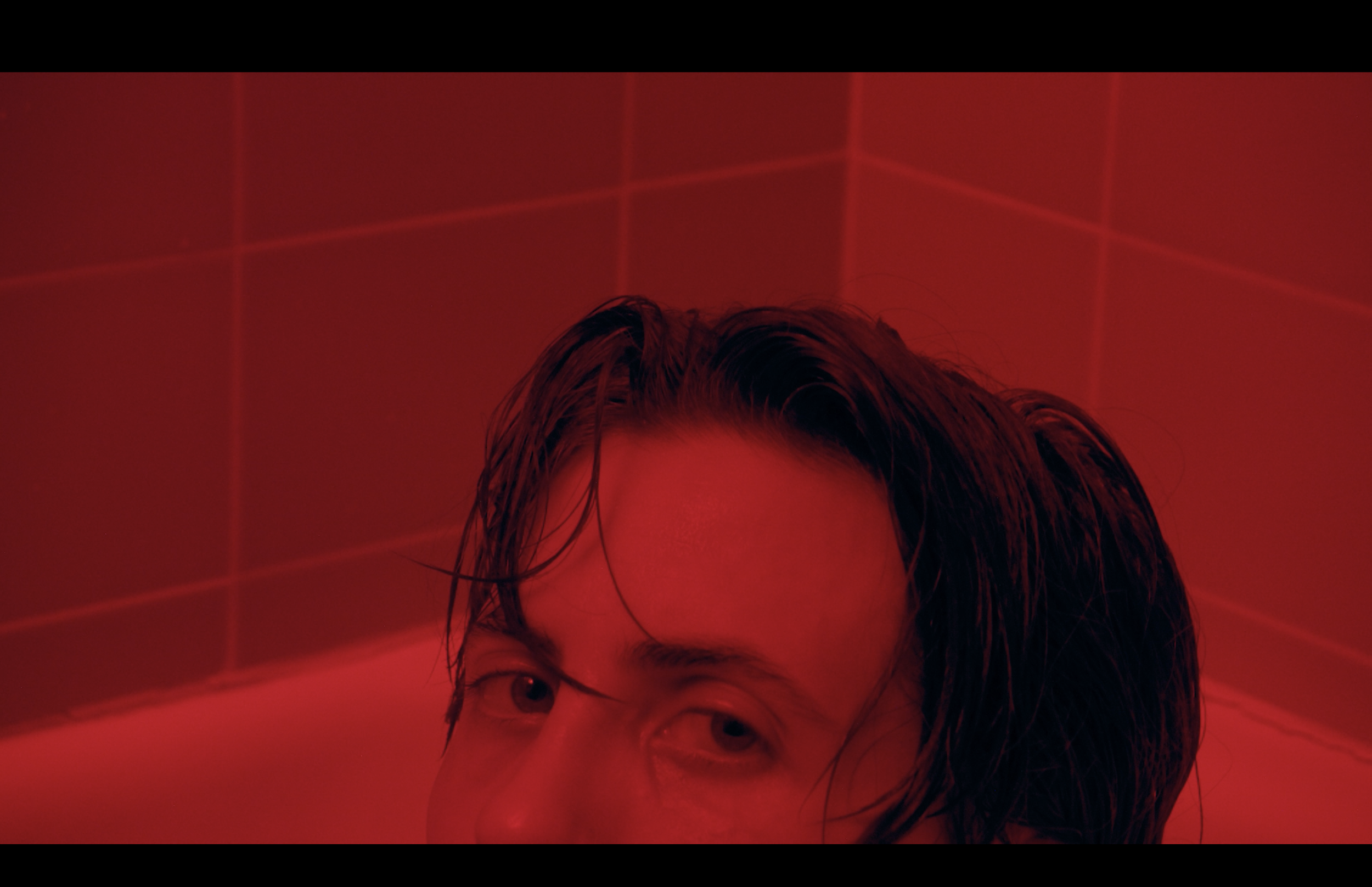 Close-up of a person's face with wet hair, partially visible, against a red grid-lit background.